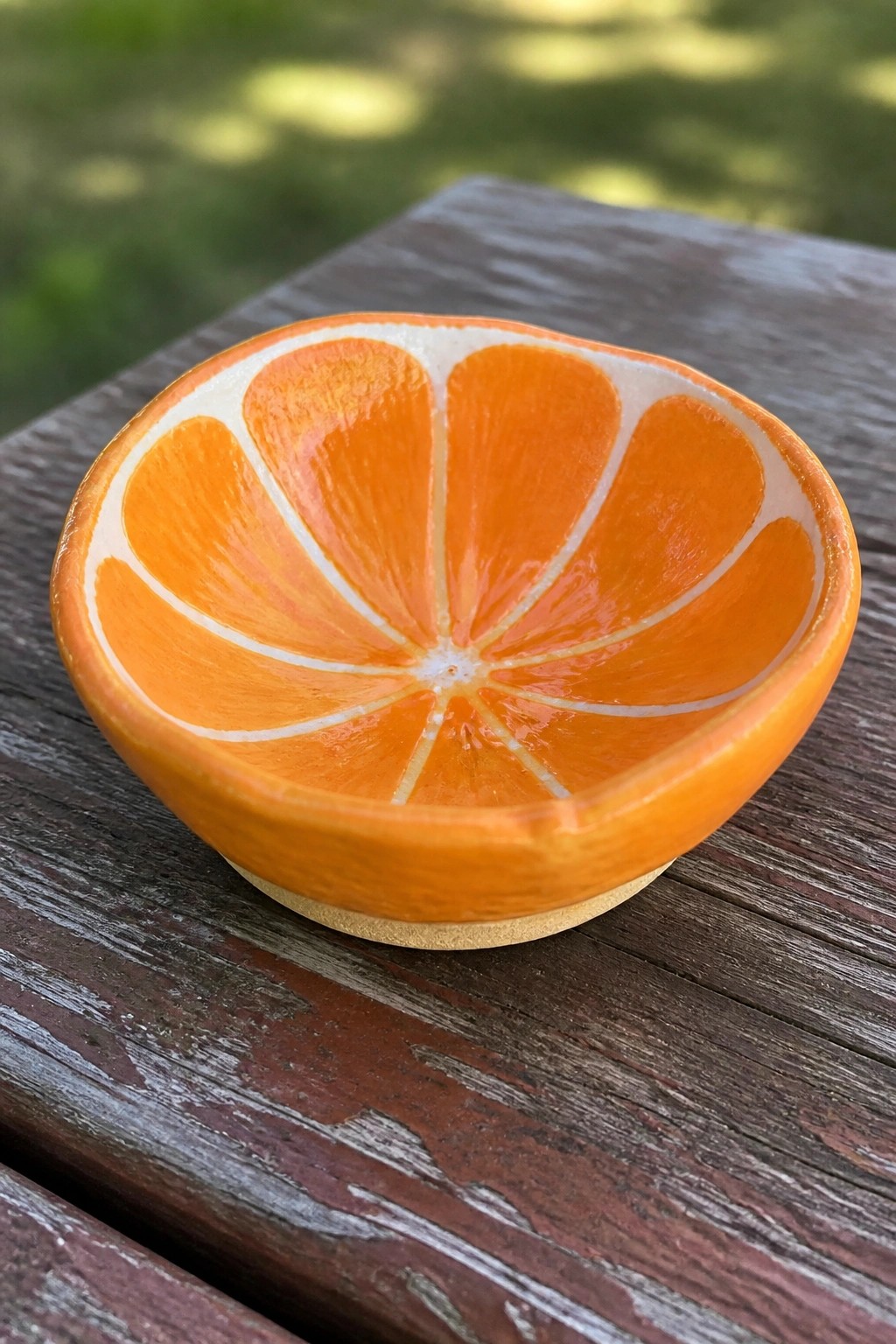 Orange half bowl with segmented design on weathered wooden table outdoors