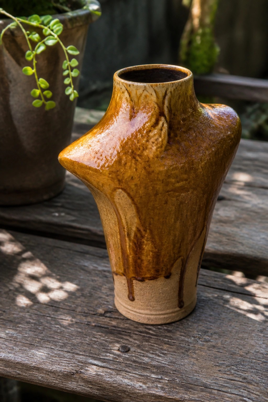 Amber-brown glazed ceramic vase with dripping texture on wooden table