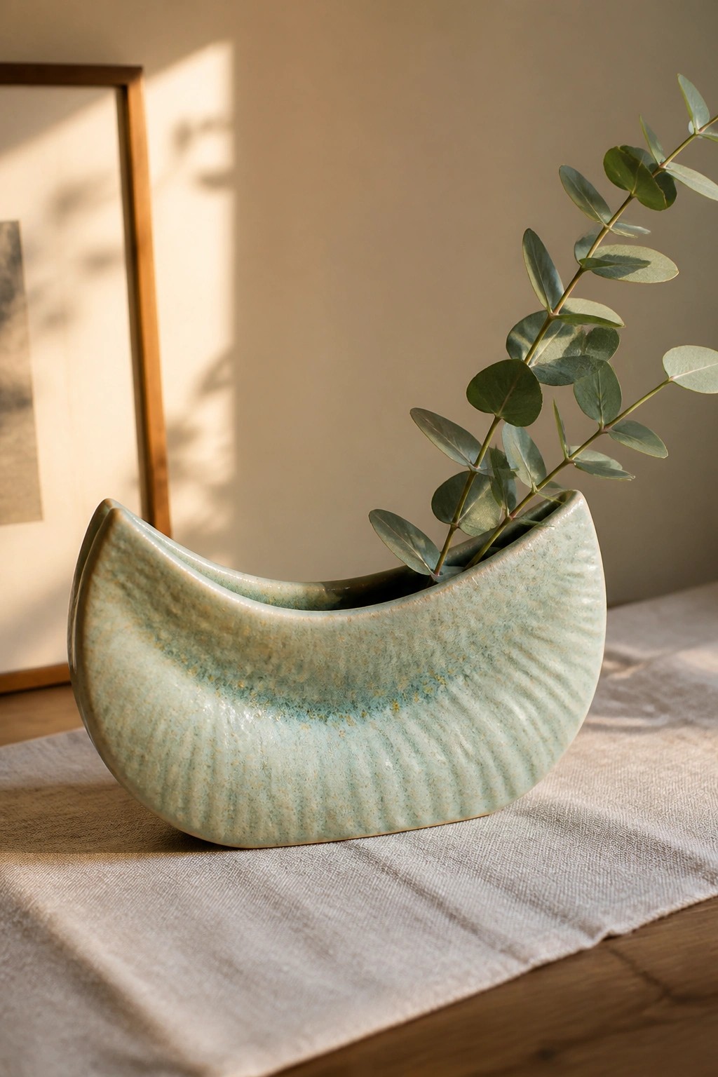 Ribbed light green ceramic crescent vase holding eucalyptus on linen cloth