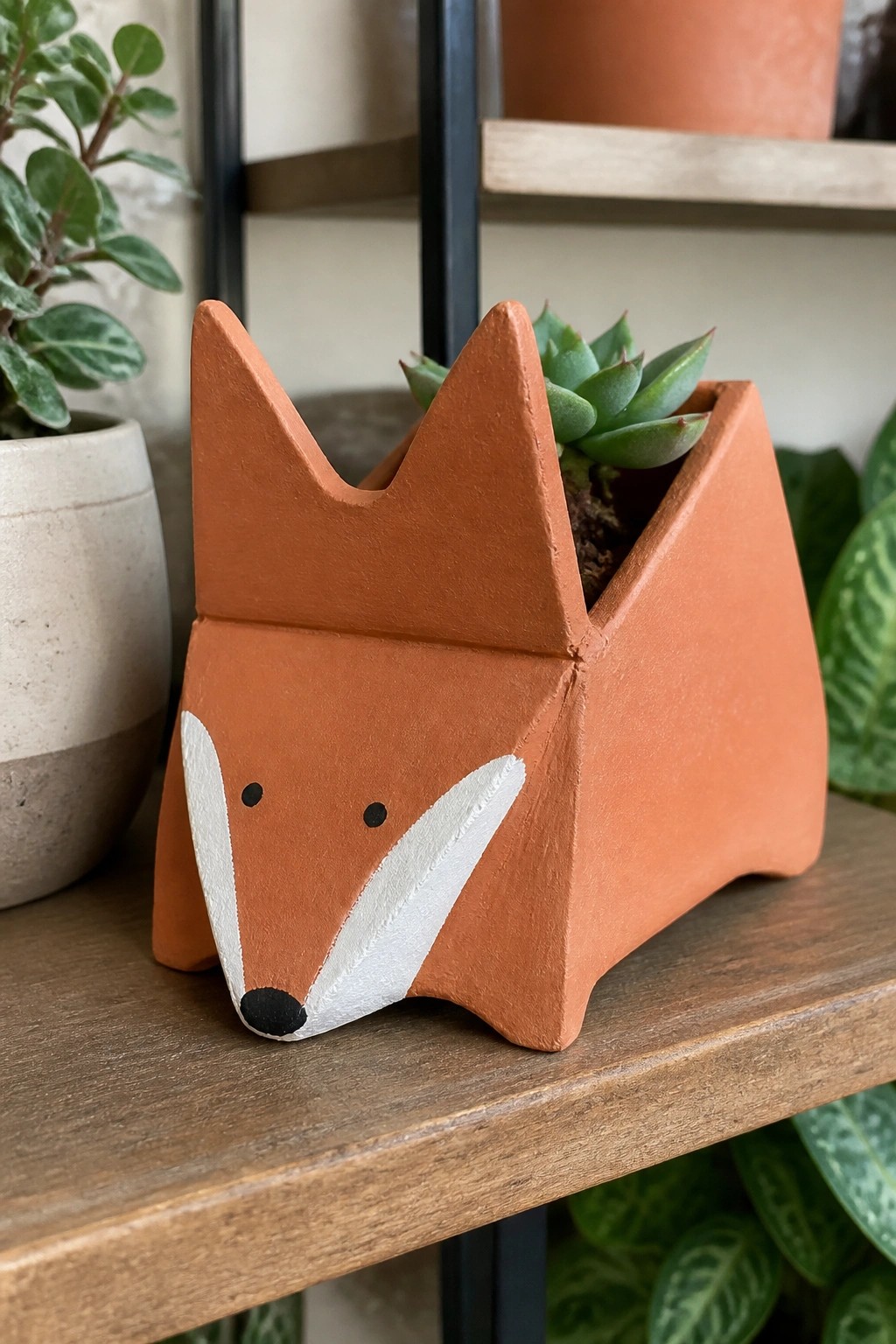 Terracotta fox-shaped planter with white face holding a green succulent on wood