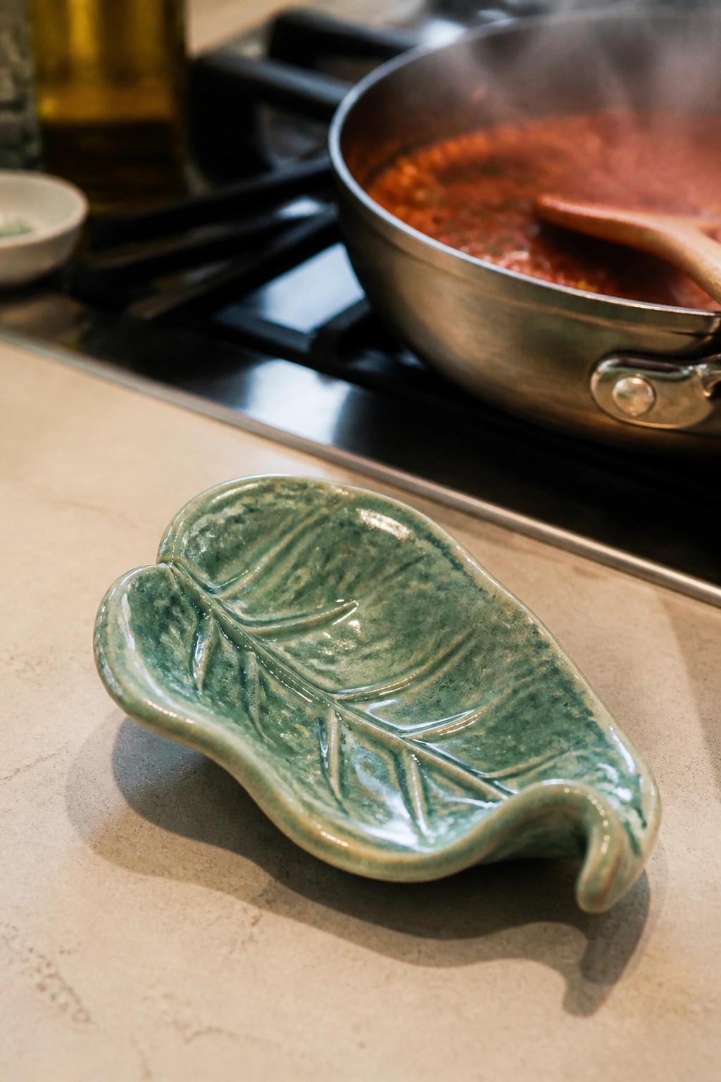 Green ceramic leaf dish on countertop beside pot of simmering red sauce