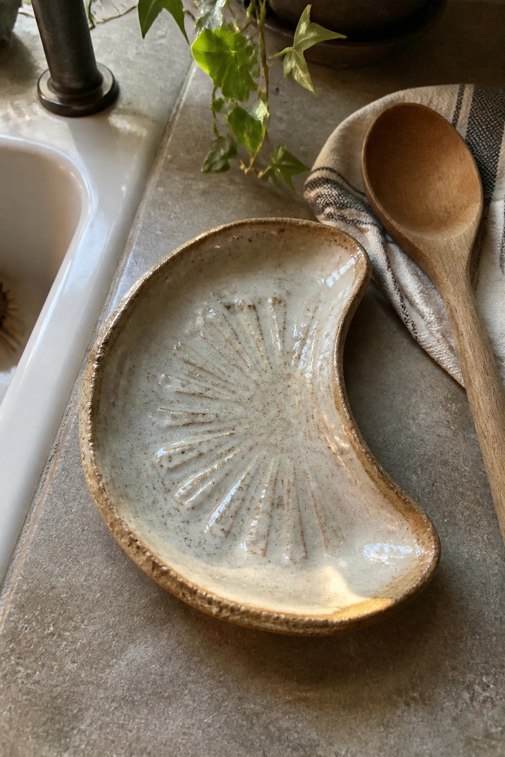 Cream ceramic dish with sunburst pattern beside wooden spoon on countertop