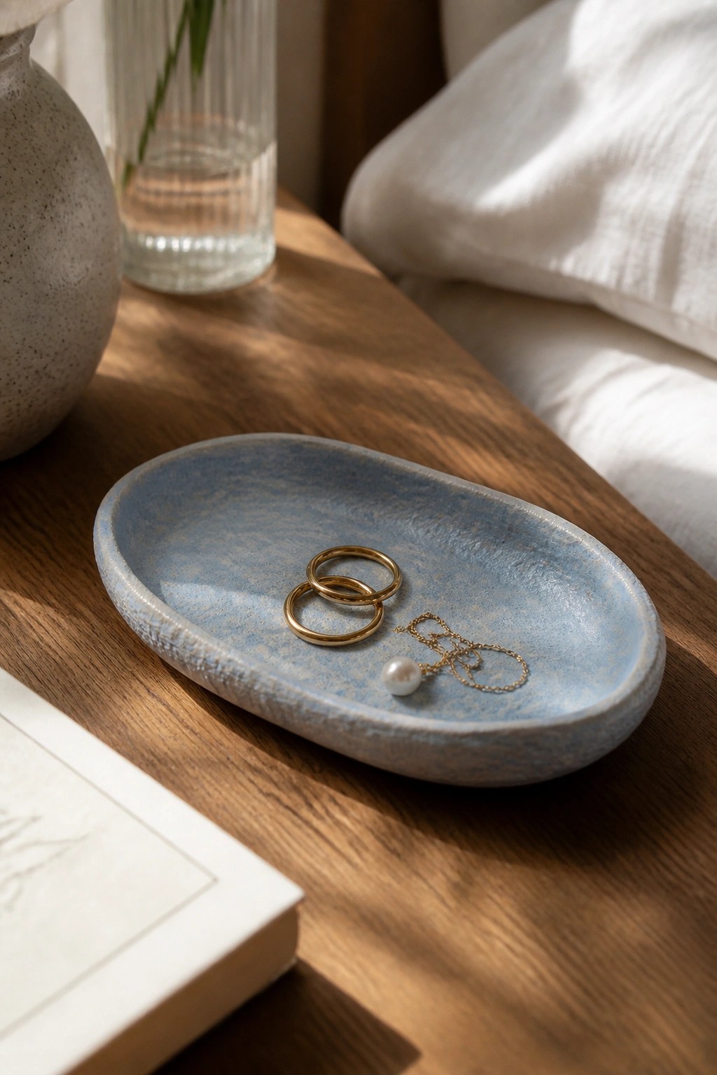 Blue ceramic tray with gold rings and pearl necklace on wooden table