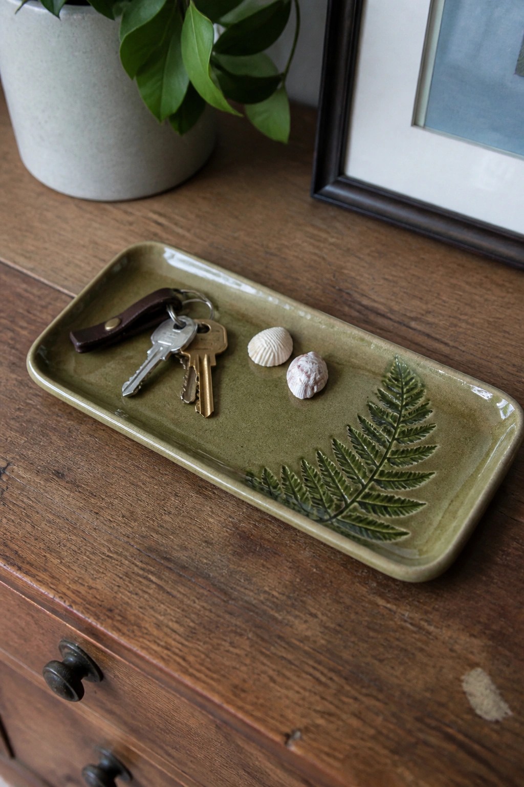 Green fern-embossed tray holding keys and seashells on wooden dresser