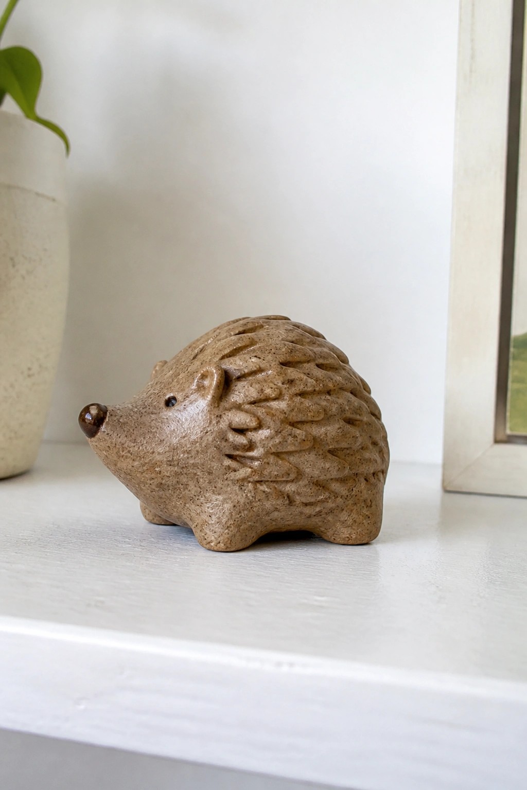Small brown ceramic hedgehog figurine with textured spines on white shelf