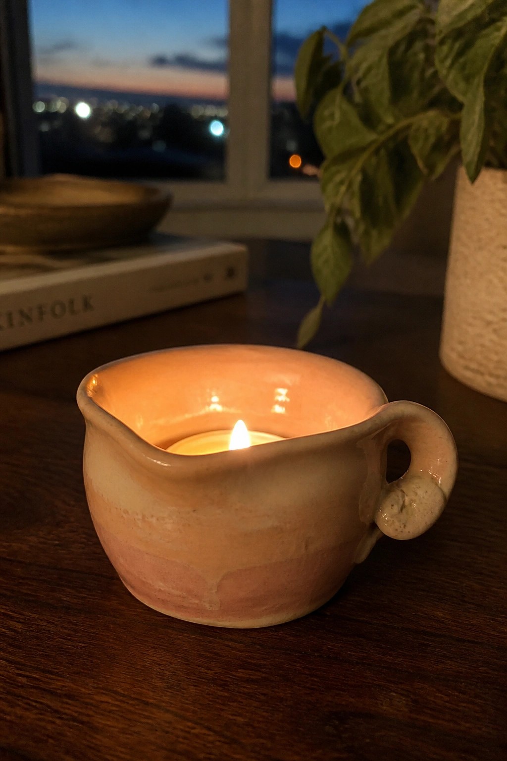 Lit candle in a pink marbled ceramic creamer on a wooden table at dusk