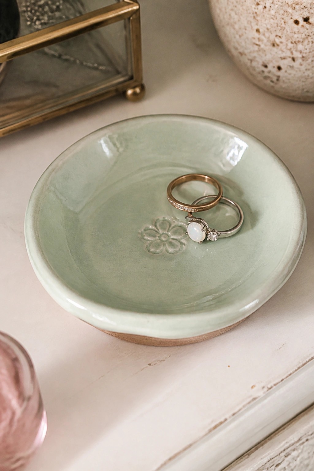 A light green ceramic dish with a flower imprint holding two rings on a white surface.