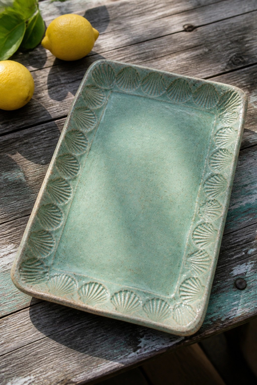 Seafoam green ceramic tray with scallop shells on weathered wood beside lemons