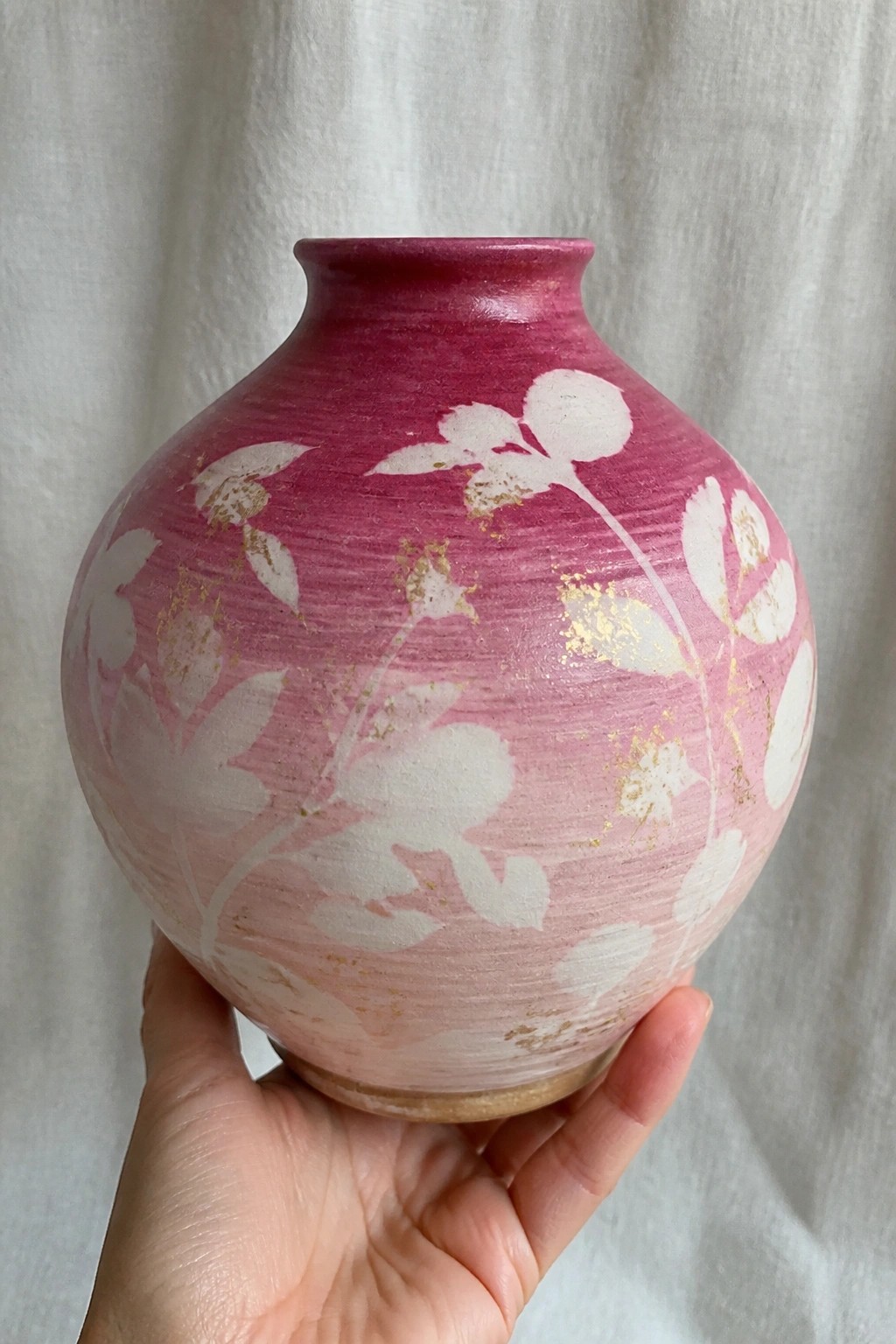 Hand holding round pink vase with white flowers and gold accents