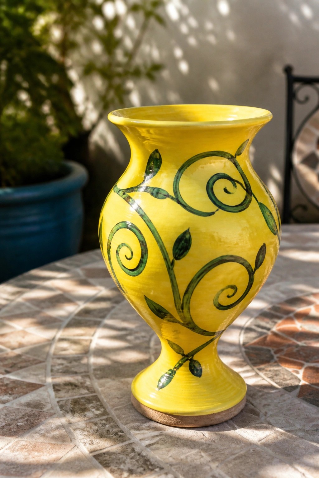 Yellow ceramic vase with green vine swirls on sunlit mosaic table