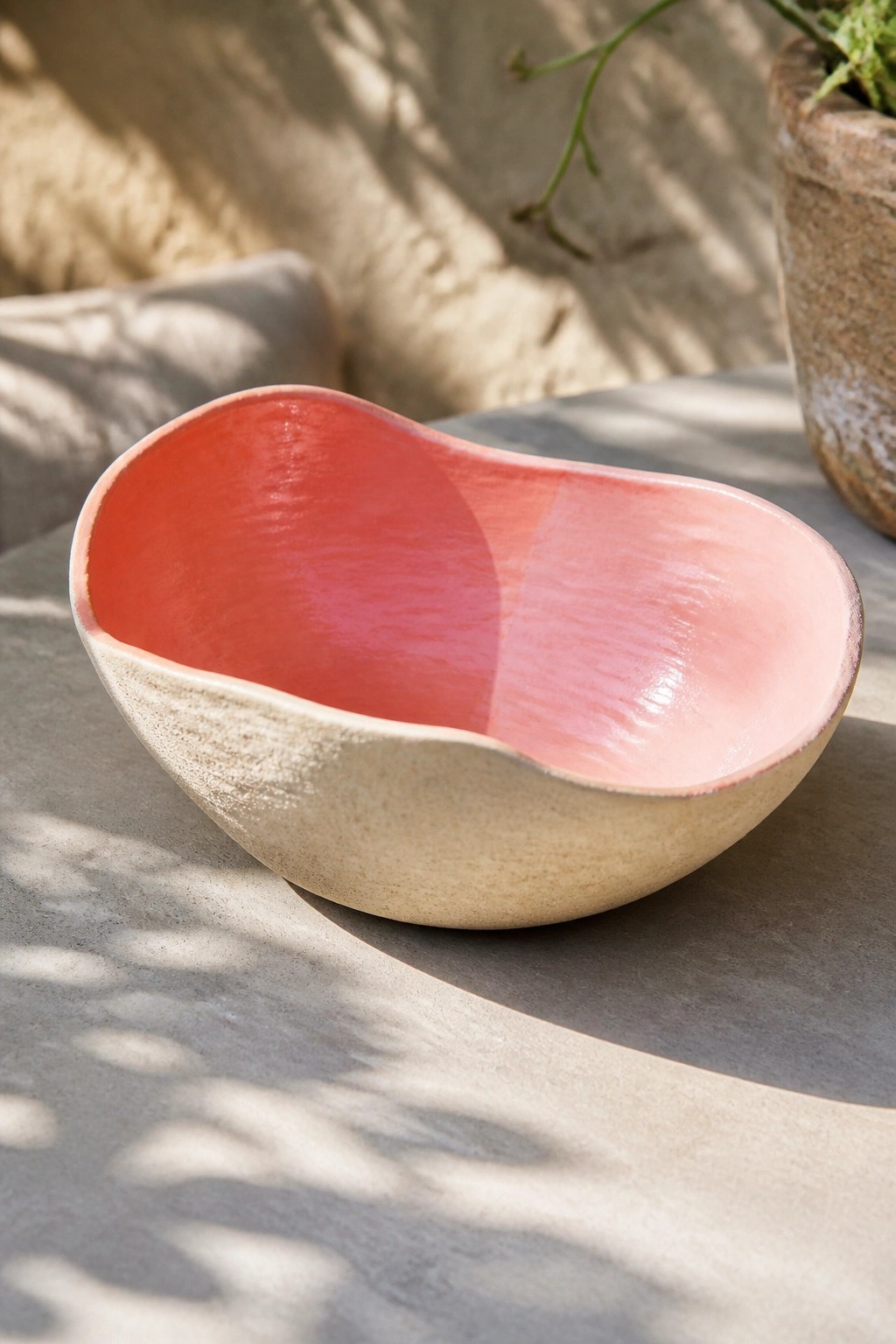 Organic ceramic bowl with glossy pink-red interior and textured beige exterior in sunlight