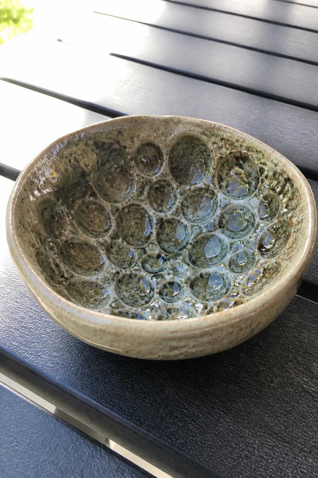 Textured green ceramic bowl with circular indentations on dark wooden table