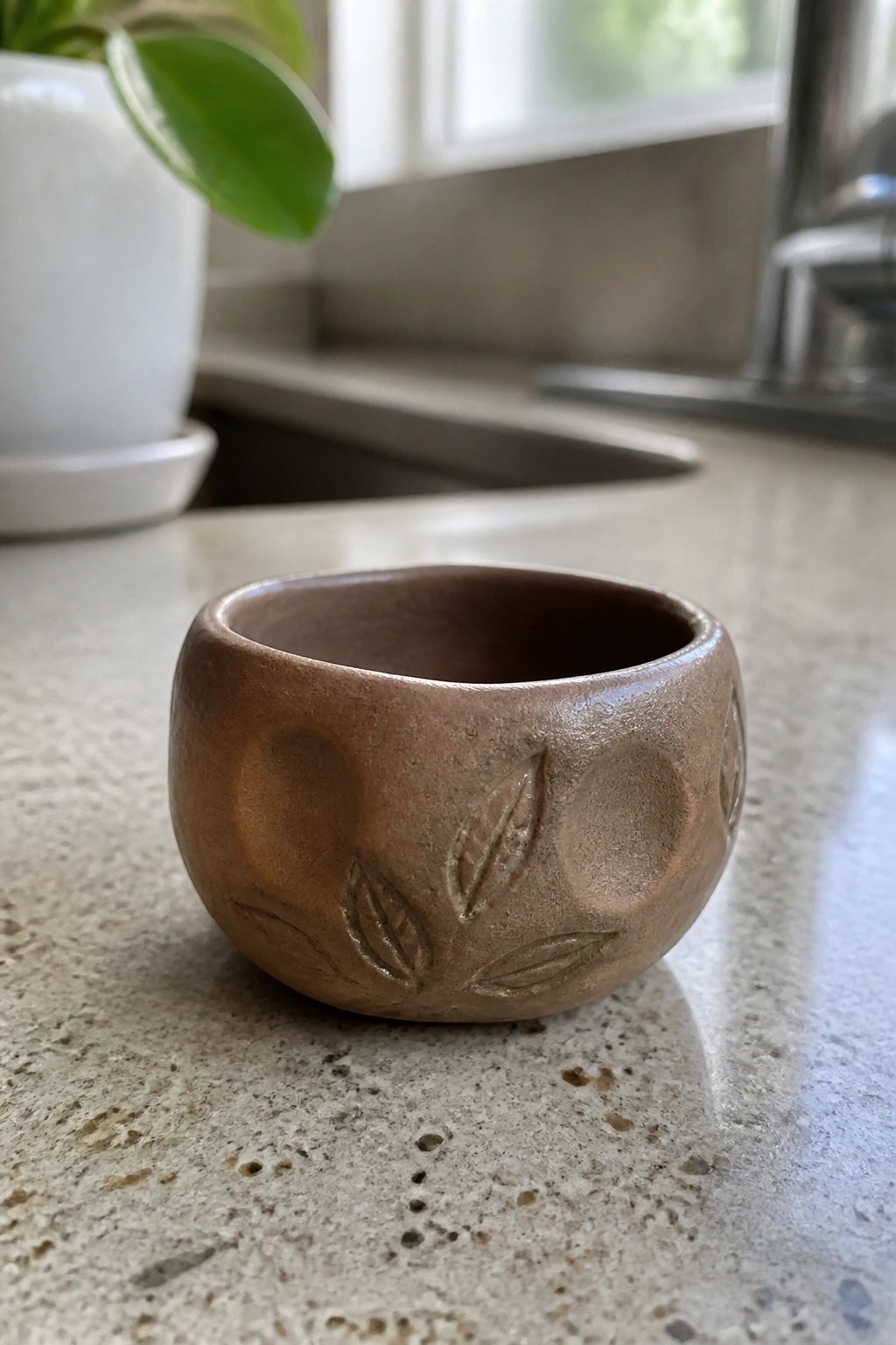 Small brown ceramic bowl with leaf imprints on speckled kitchen countertop