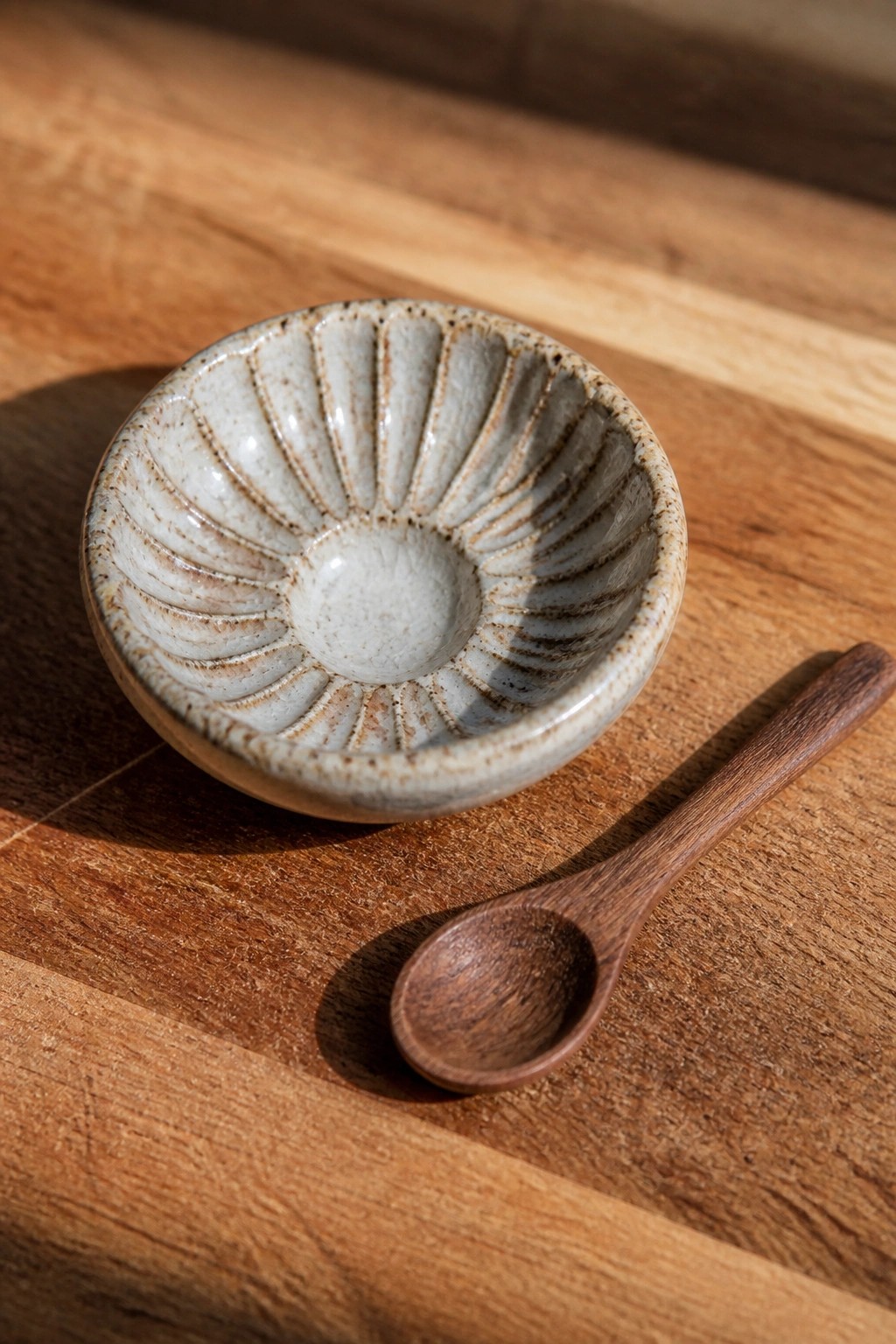 Ceramic bowl with fluted interior beside wooden spoon on wooden surface