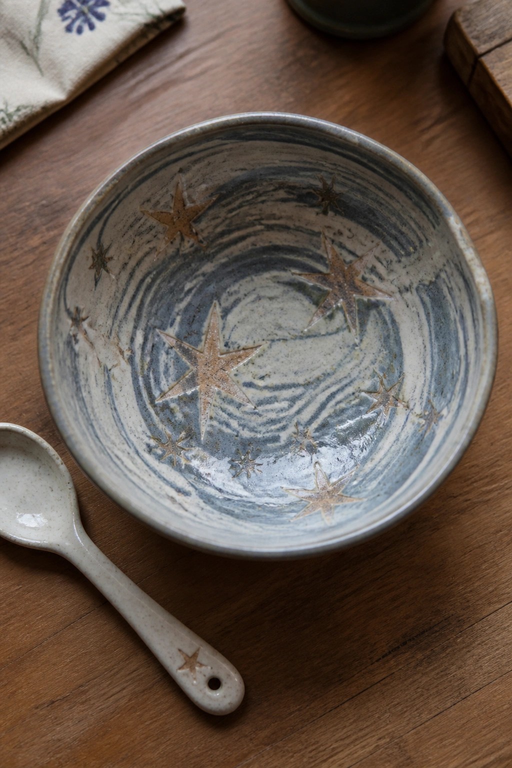 Blue-swirled ceramic bowl with brown stars beside star-handled spoon on wood.