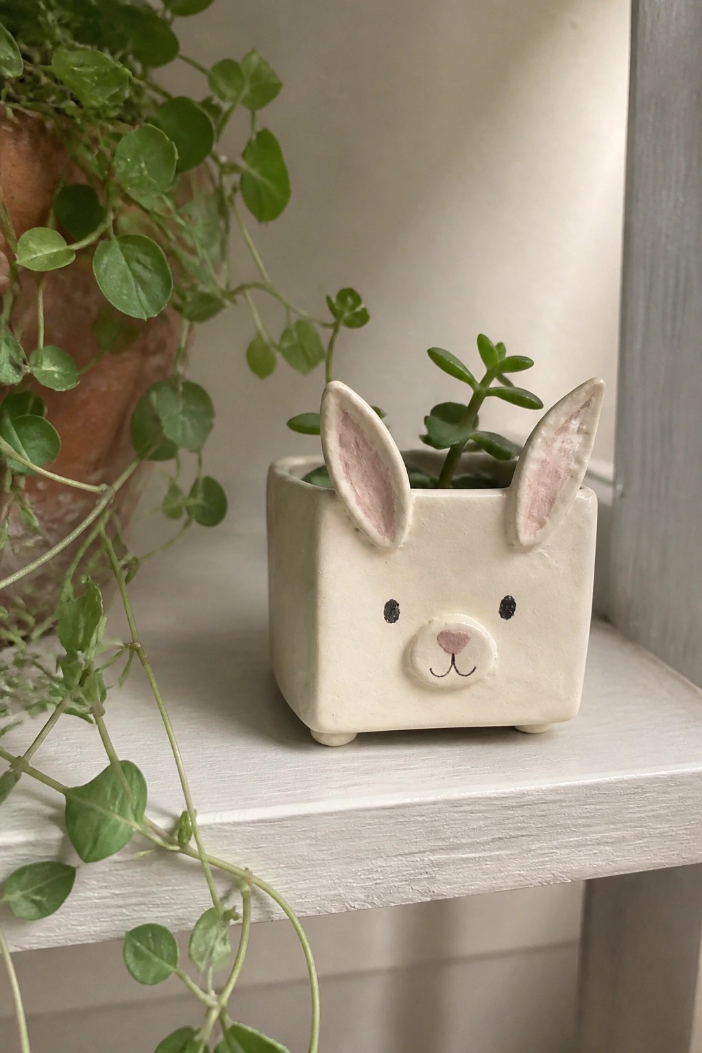 White ceramic bunny planter with pink ears holding succulent on shelf