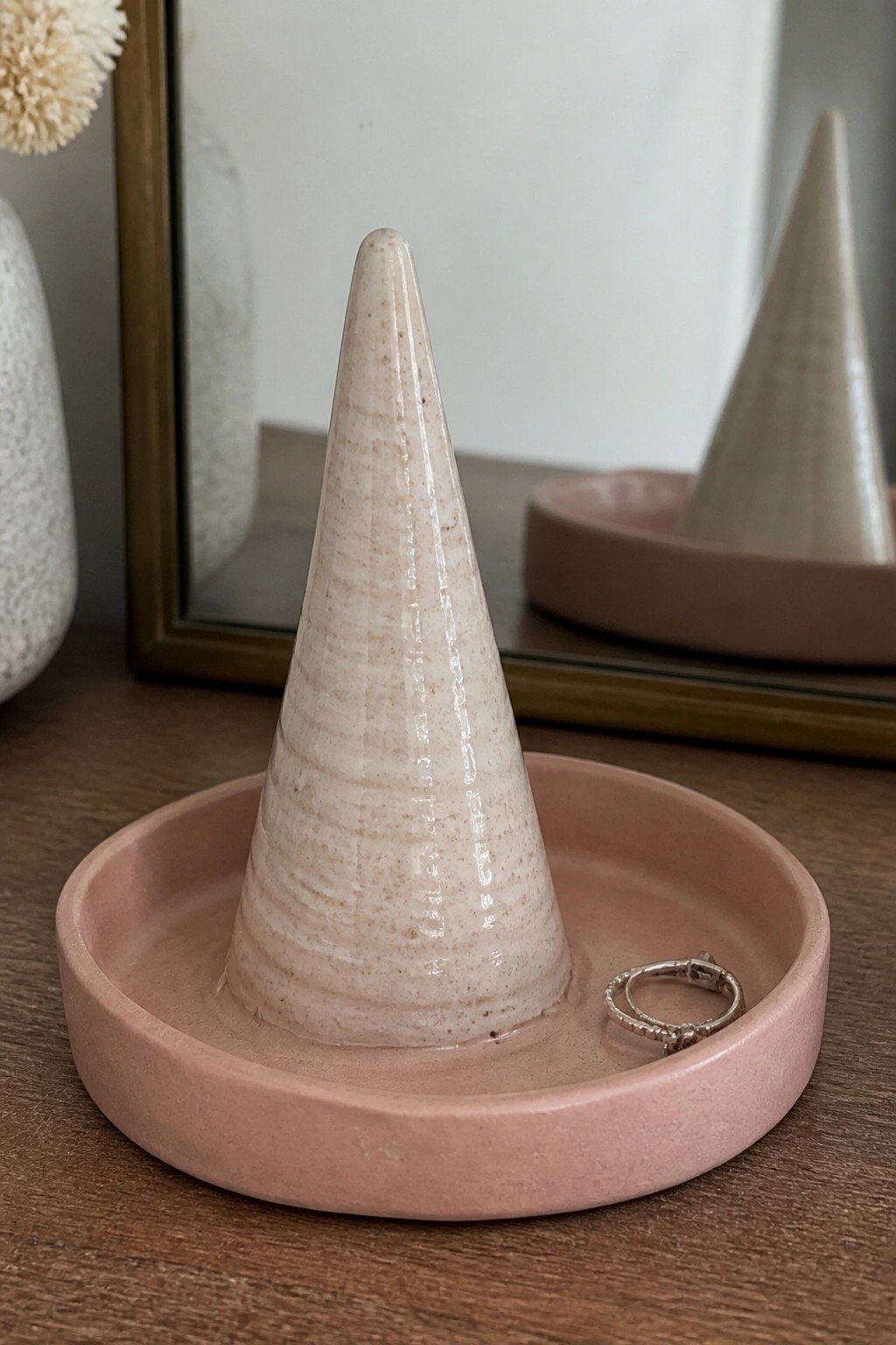 Ceramic ring holder with pink tray and central cone, silver ring resting on the tray.