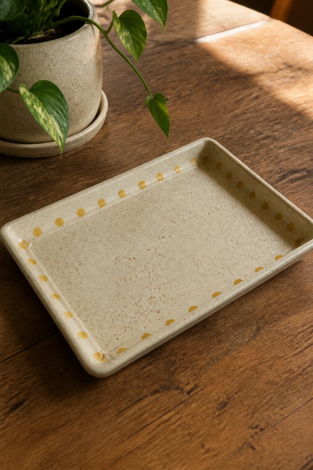 Beige speckled tray with yellow dots along rim on wooden table beside plant