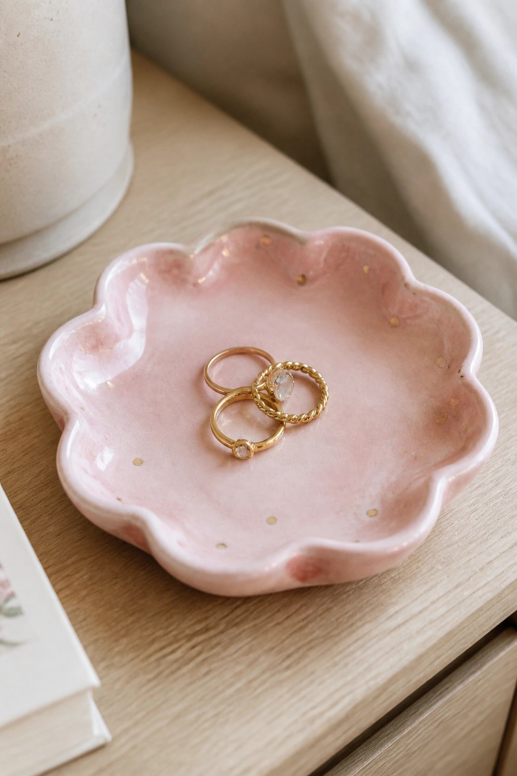 Pink scalloped ceramic dish with gold flecks holding three gold rings on wood