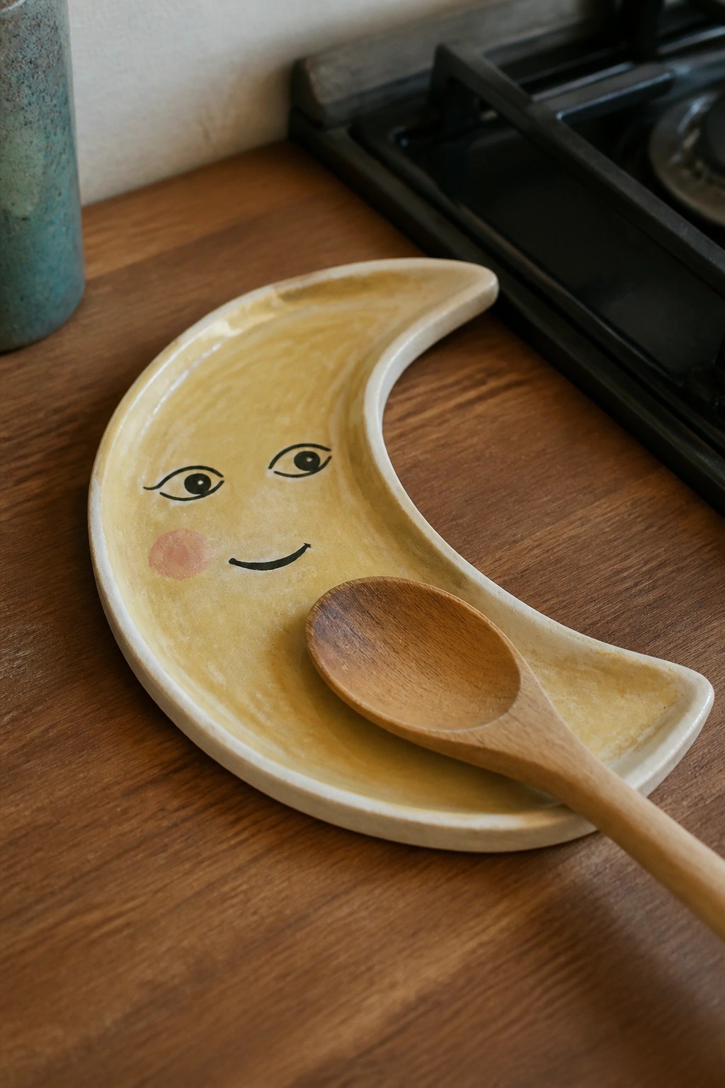 Yellow crescent moon ceramic plate with smiling face and wooden spoon on counter