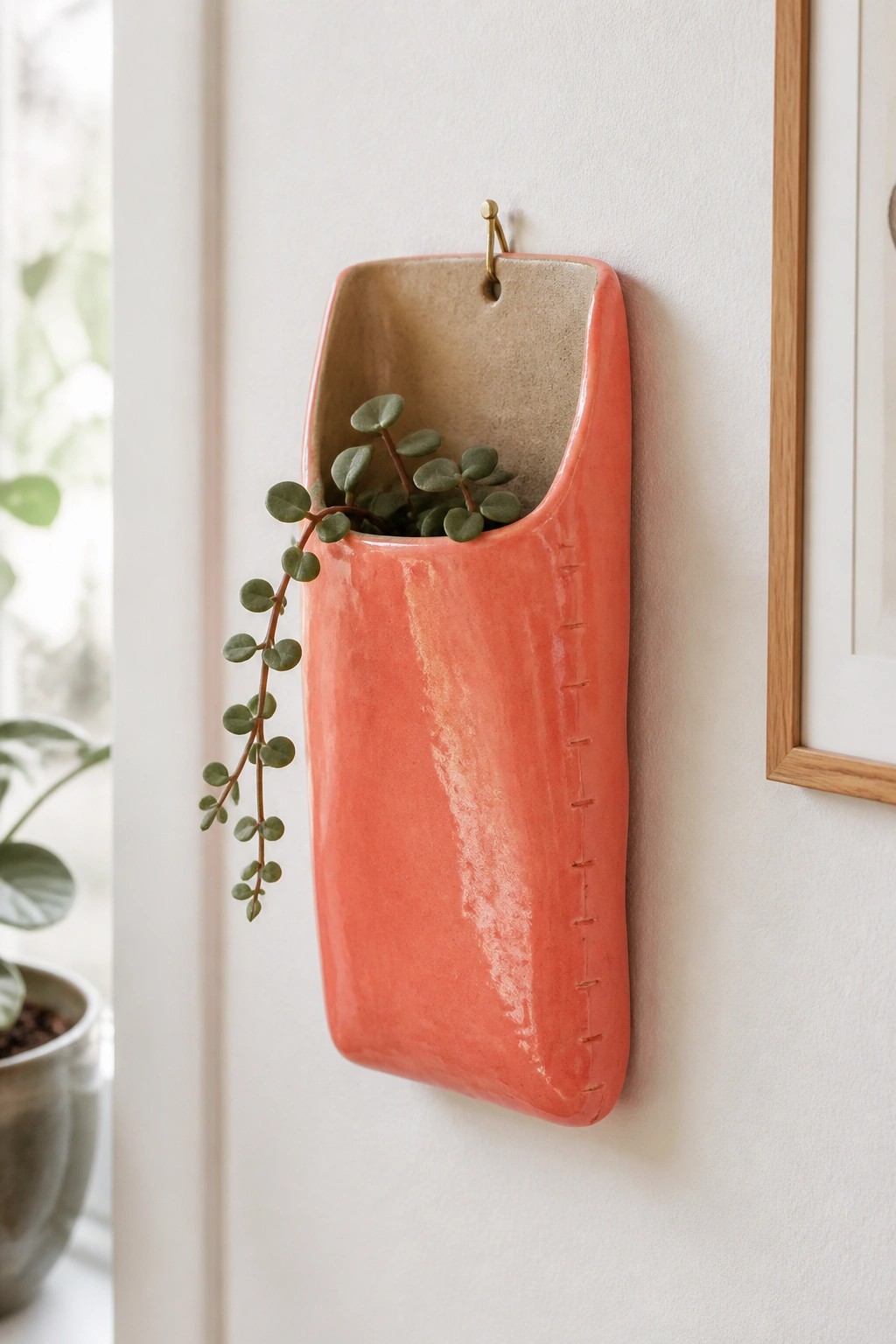 Coral ceramic wall pocket with trailing green plant on white wall.