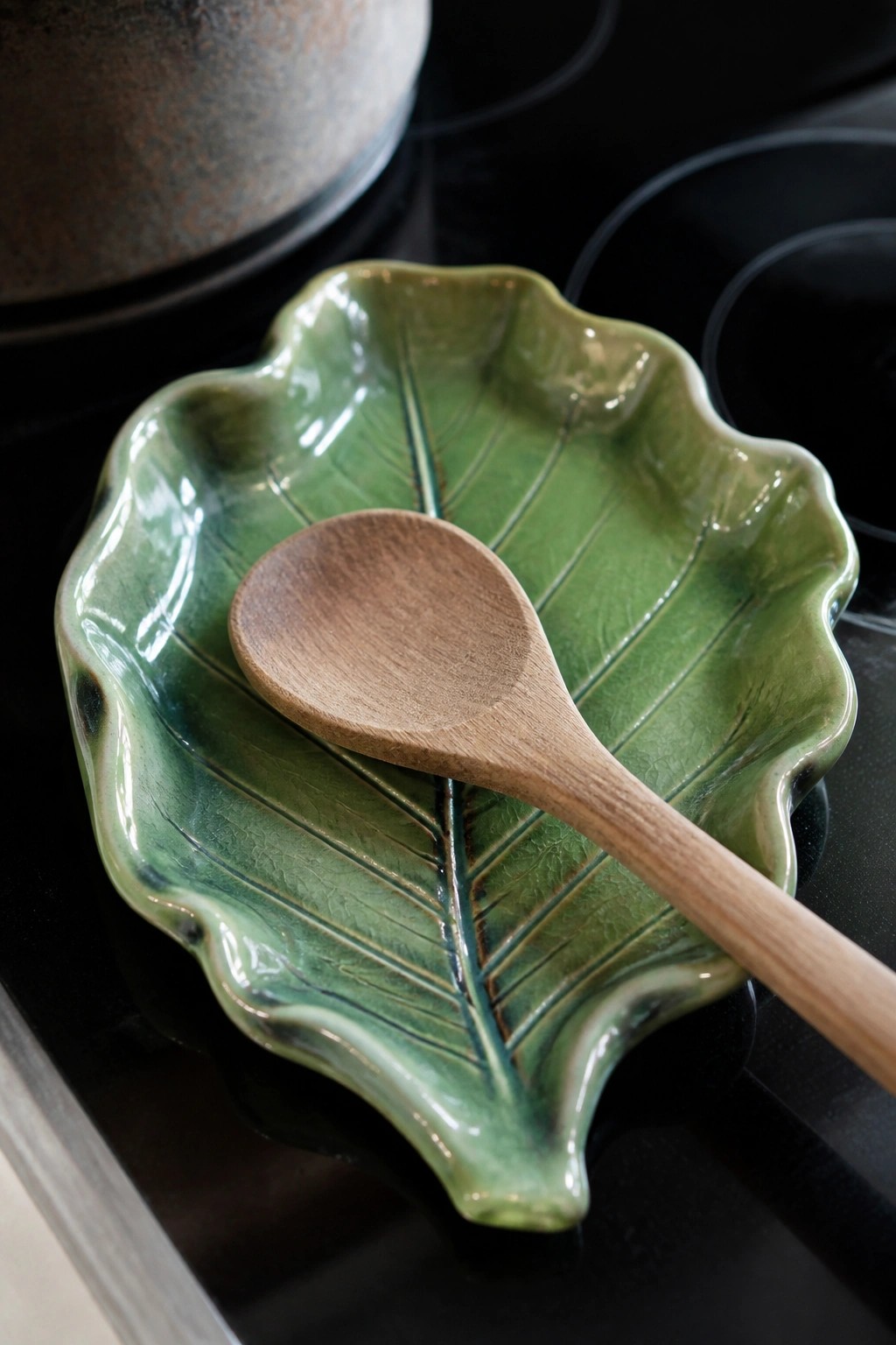 Wooden spoon rests on green ceramic leaf-shaped dish atop black stovetop.