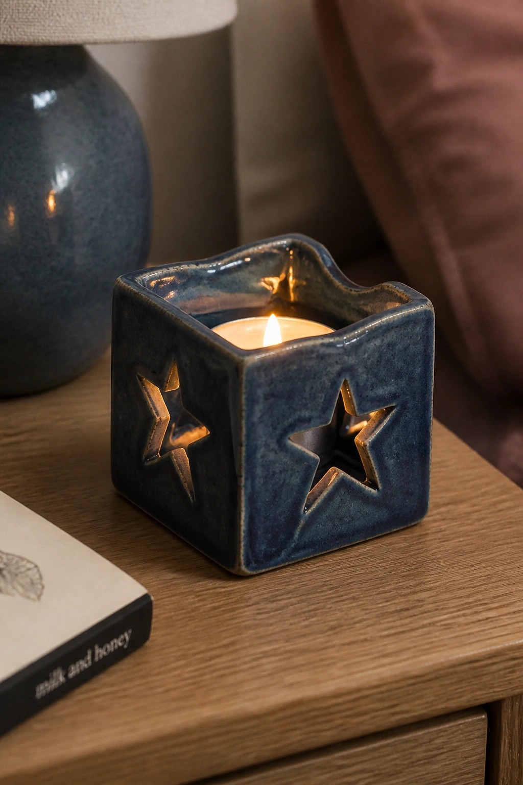 Lit candle in blue ceramic star-cutout holder beside book on wooden table