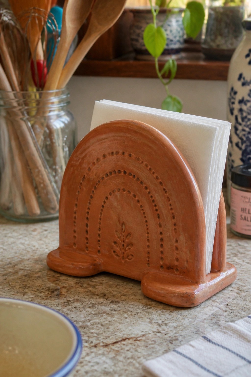 Terracotta rainbow napkin holder with white napkins on speckled kitchen countertop