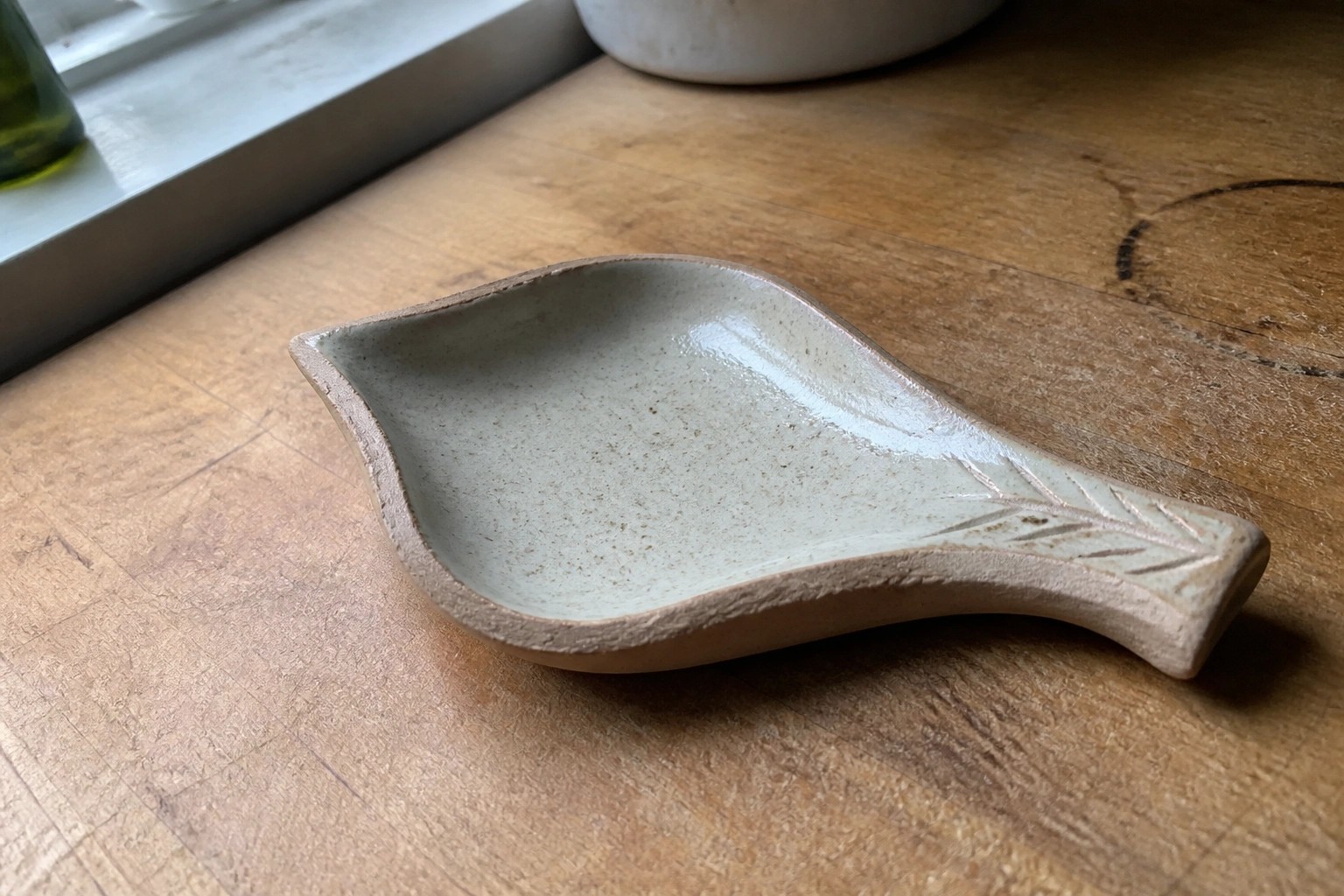 Leaf-shaped speckled ceramic dish with embossed veins on wooden table