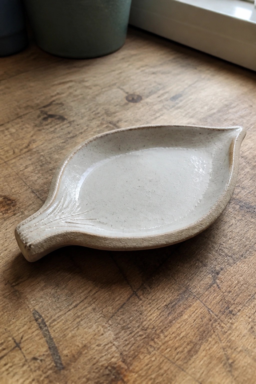 Leaf-shaped speckled ceramic dish with embossed veins on wooden table