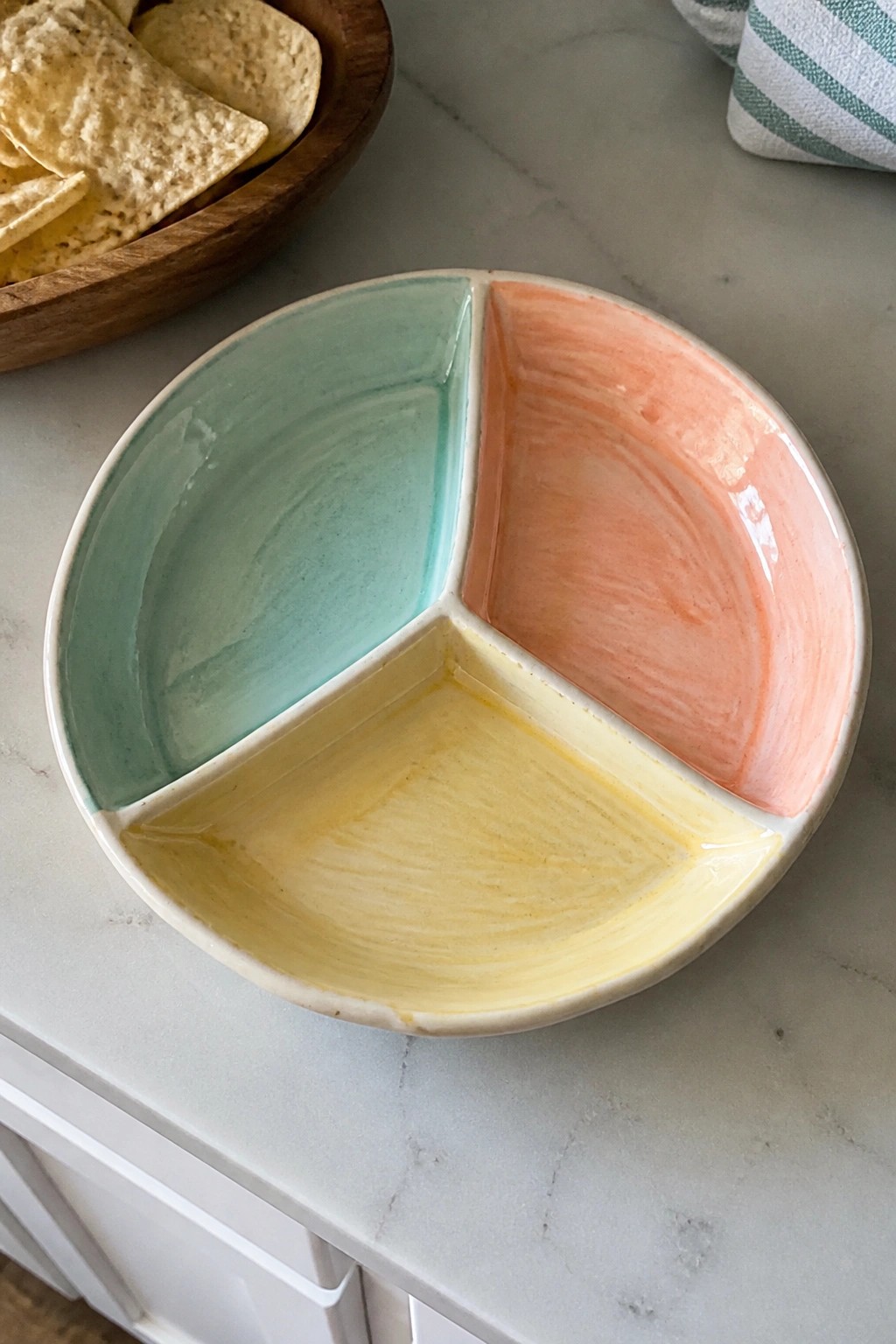 Divided ceramic bowl with mint green, yellow, and peach sections on marble near chips