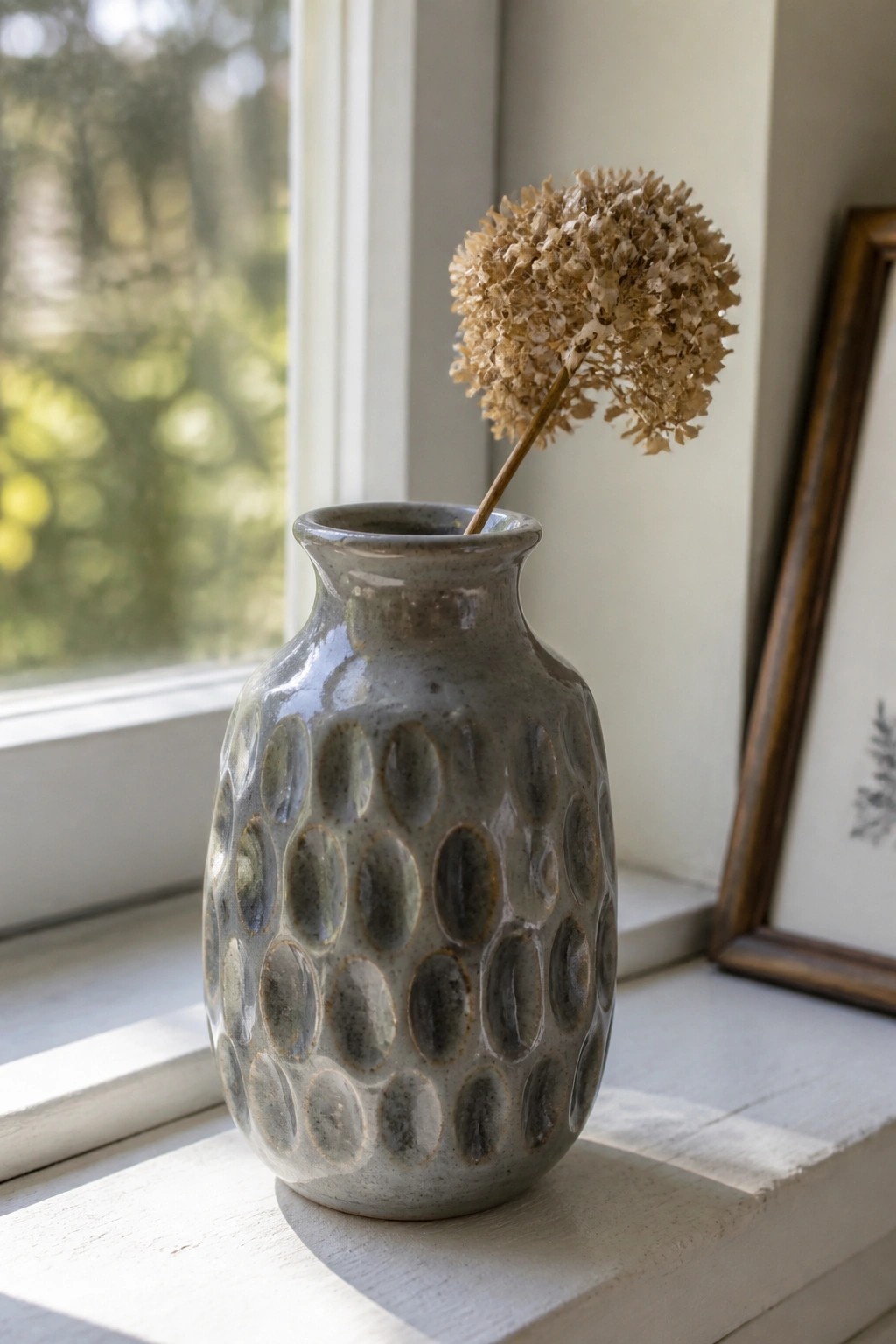 Gray dimpled ceramic vase with dried hydrangea on sunny white windowsill