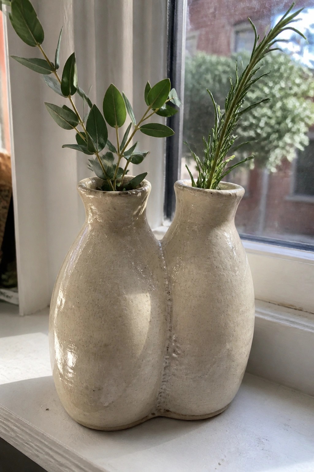 Double ceramic vase with eucalyptus and rosemary on a sunny windowsill