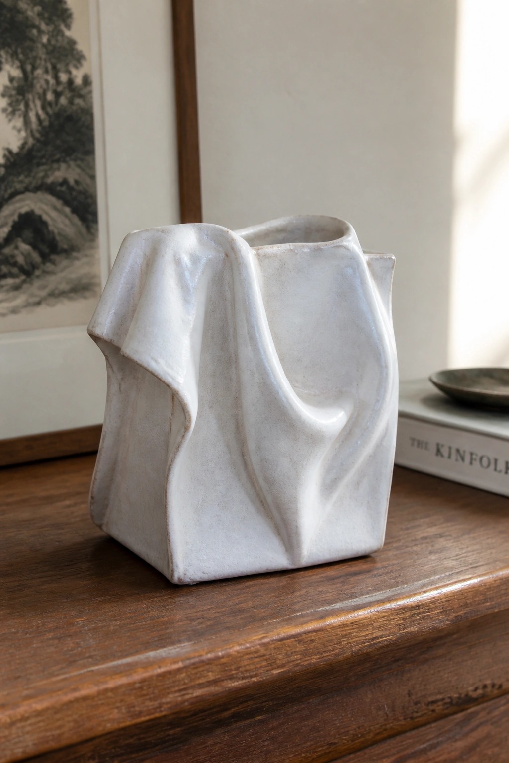 White ceramic vase with draped, fabric-like folds on wooden table