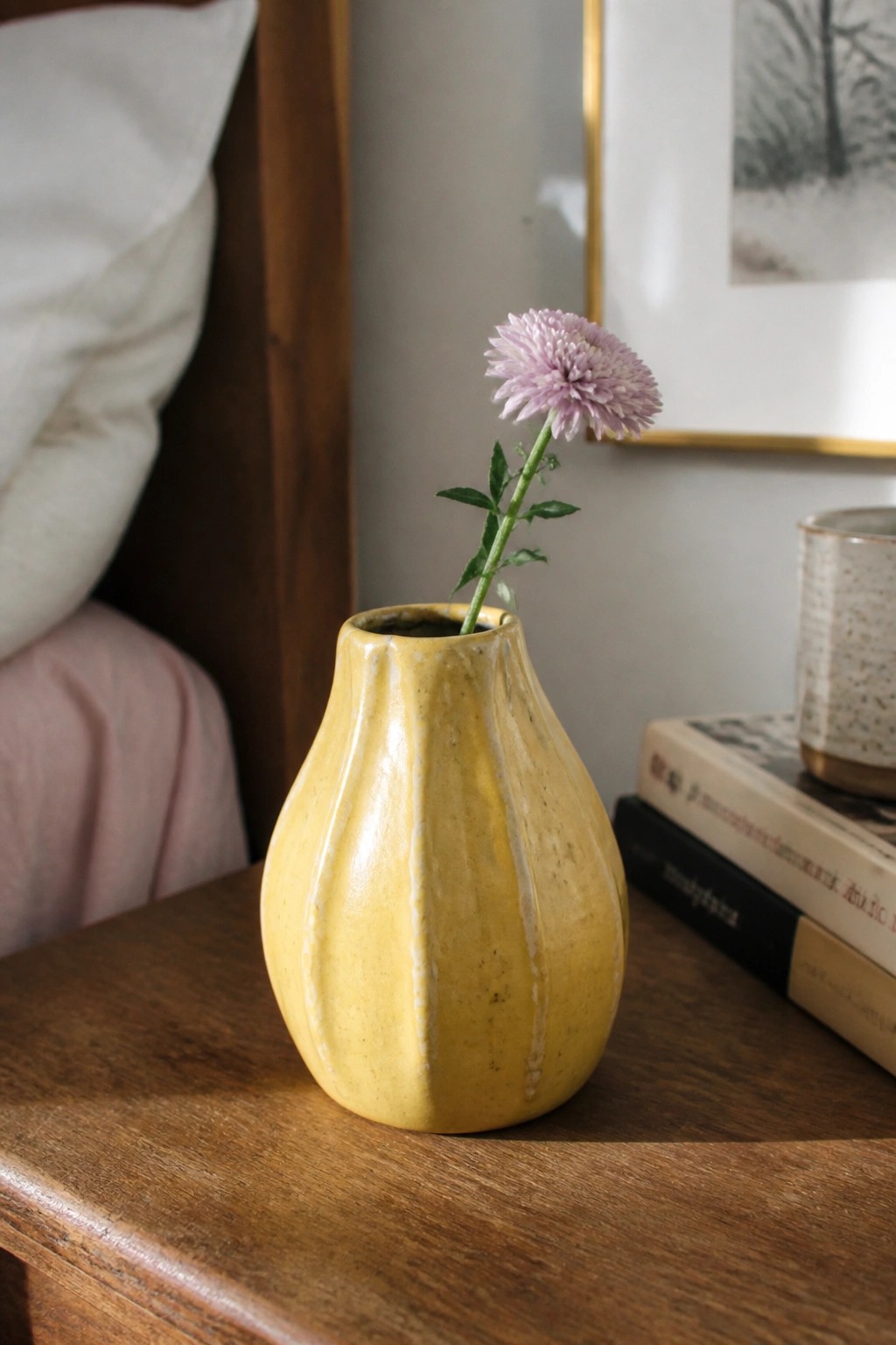 Yellow ceramic vase with purple flower on wooden table beside books
