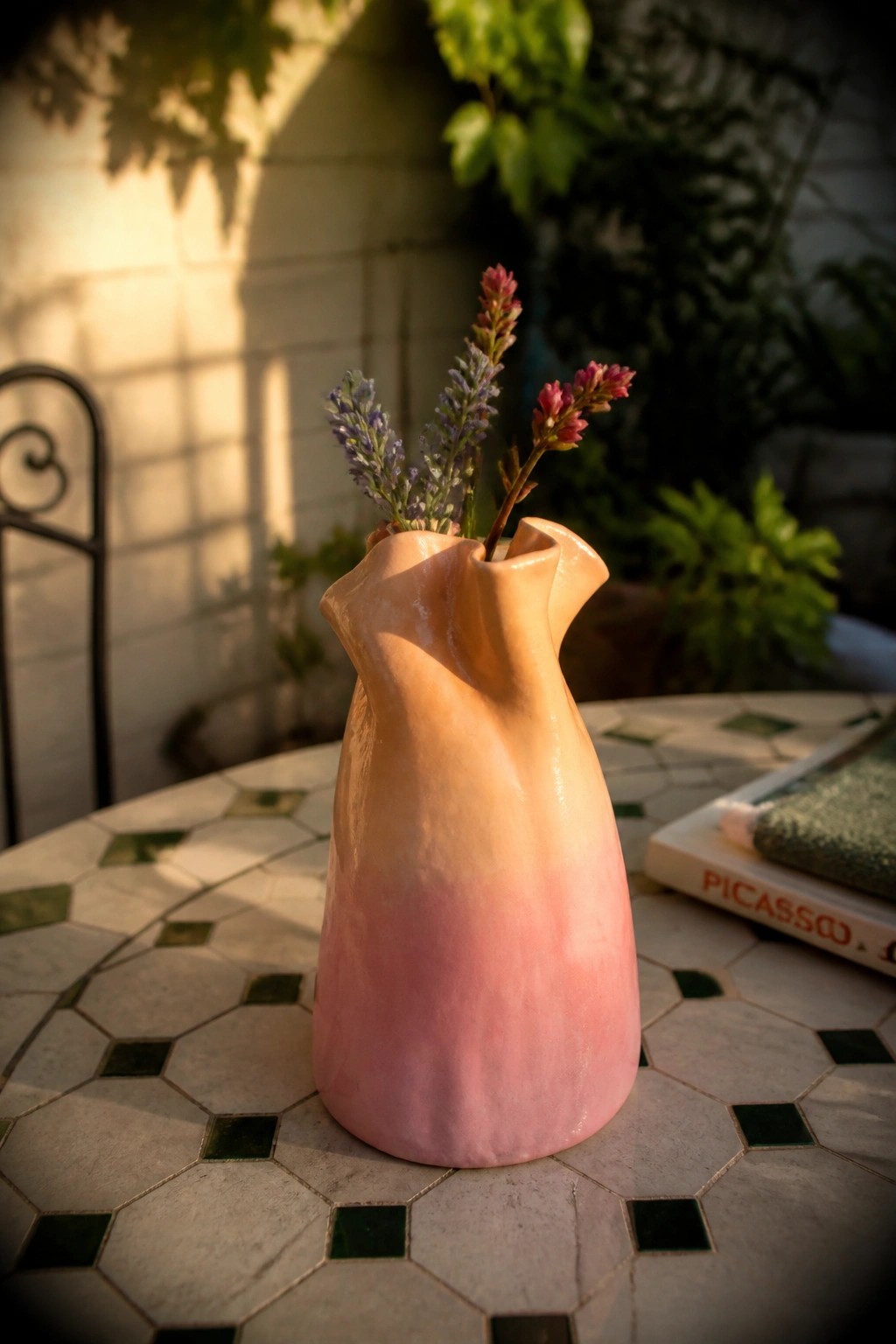 Sculptural pink gradient vase with flowers on sunlit mosaic patio table