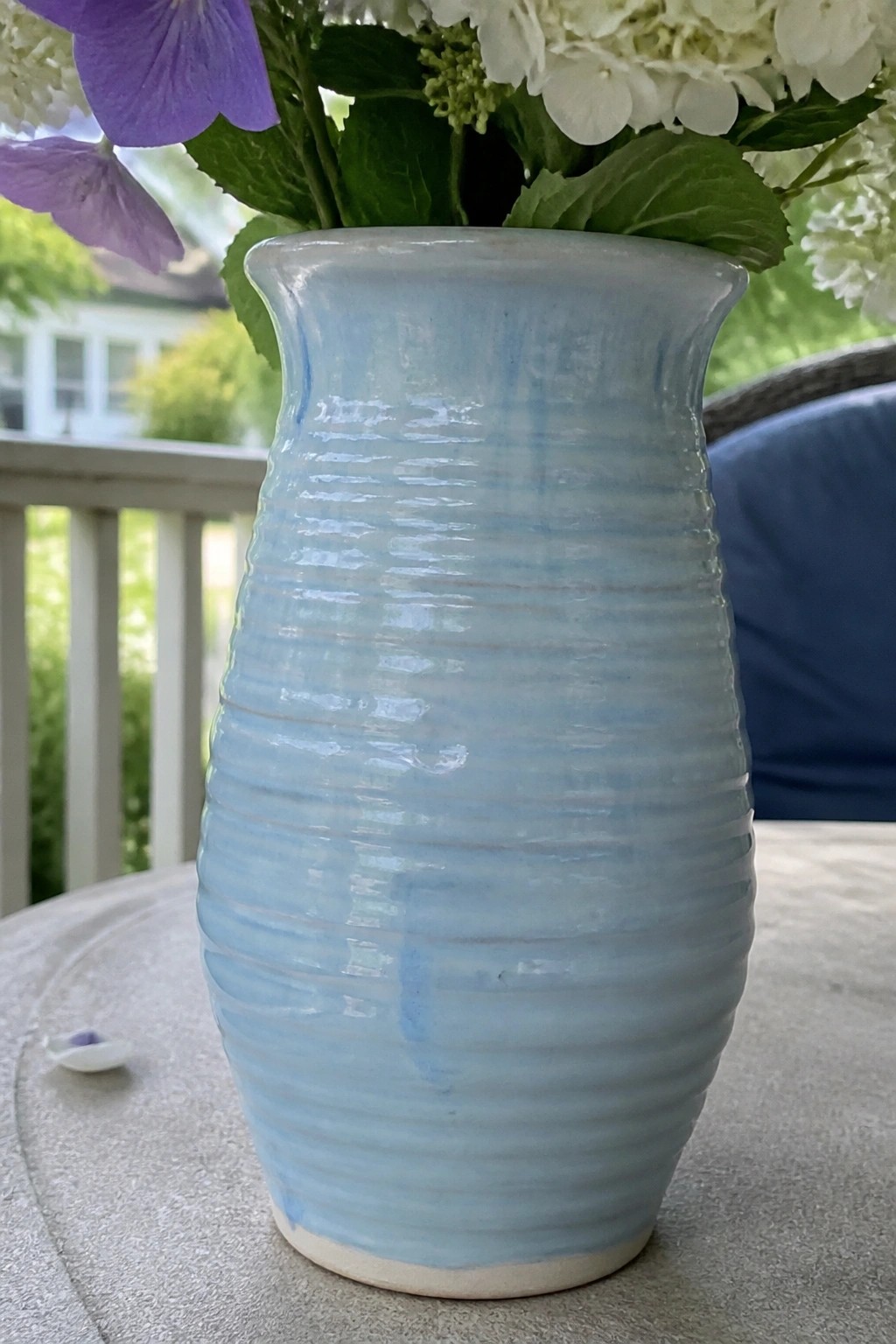 Light blue ribbed ceramic vase with white and purple flowers on outdoor table