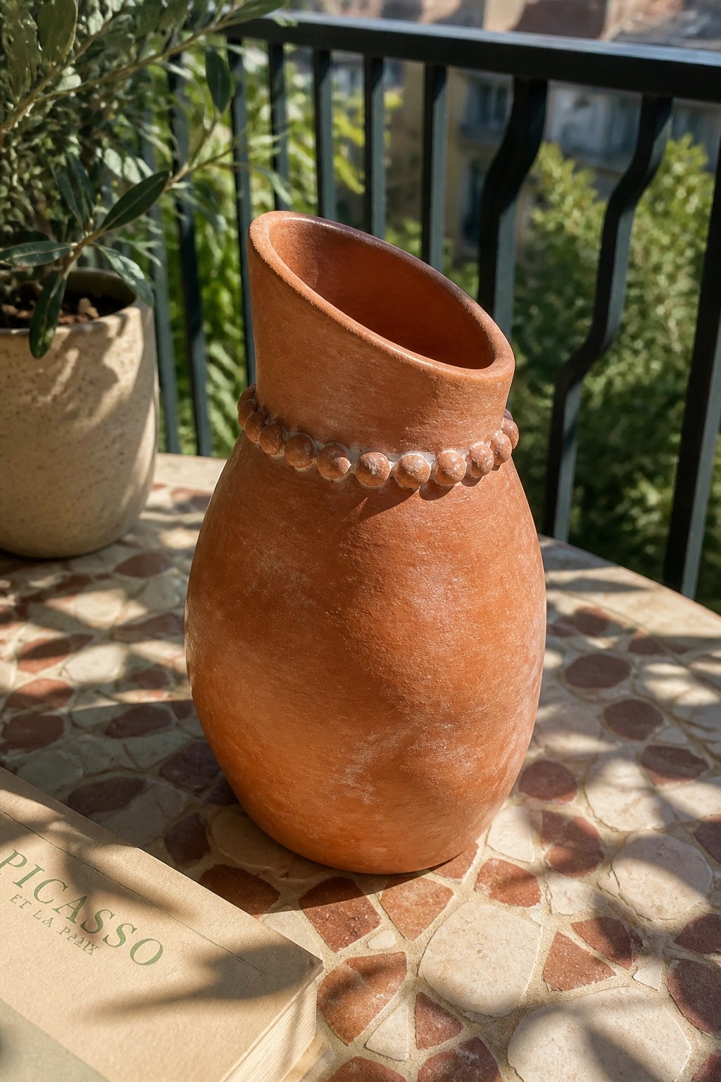 Terracotta vase with beaded neck on mosaic table beside Picasso book