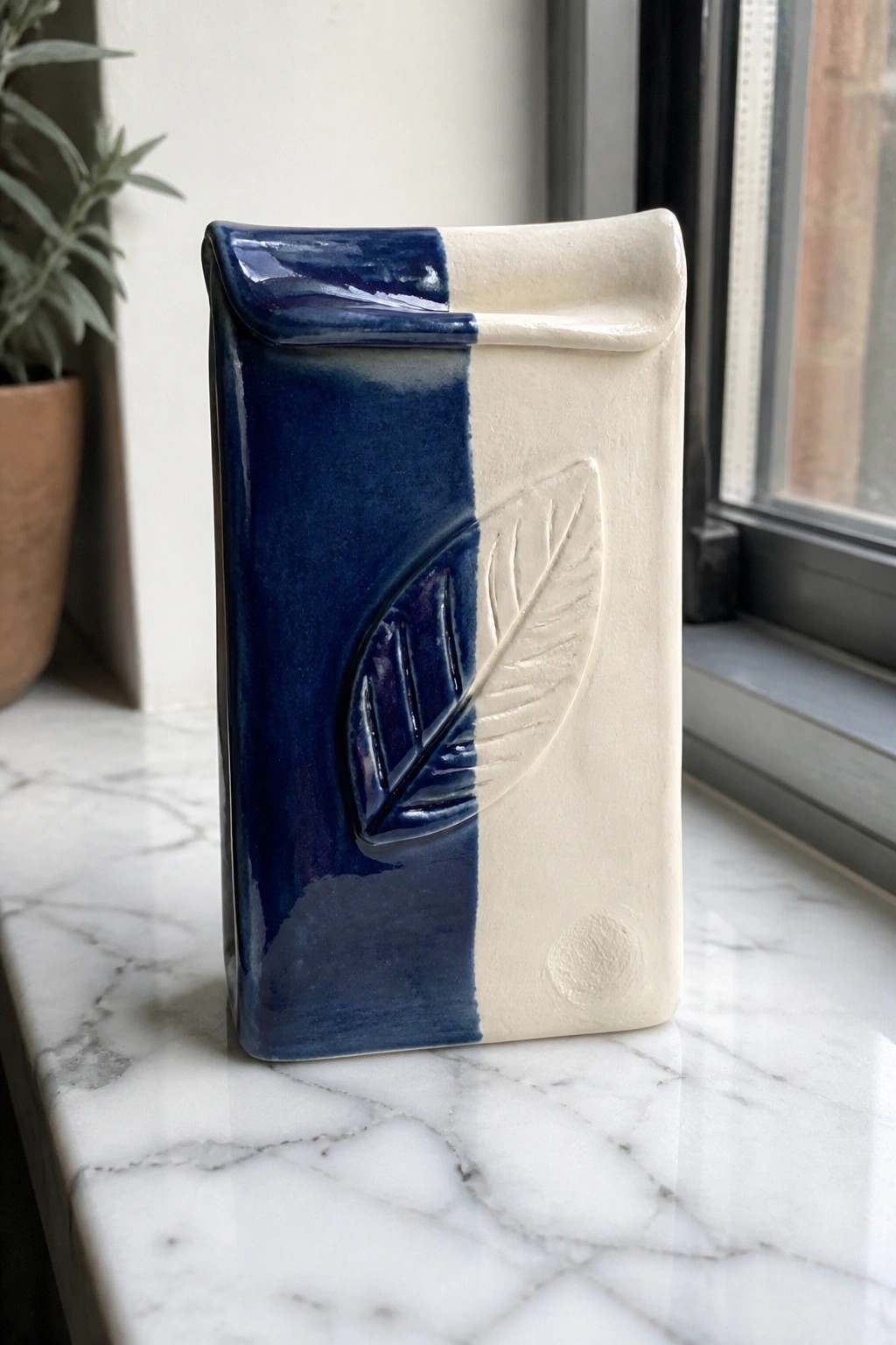 Blue and white ceramic vase with embossed leaf on marble windowsill.