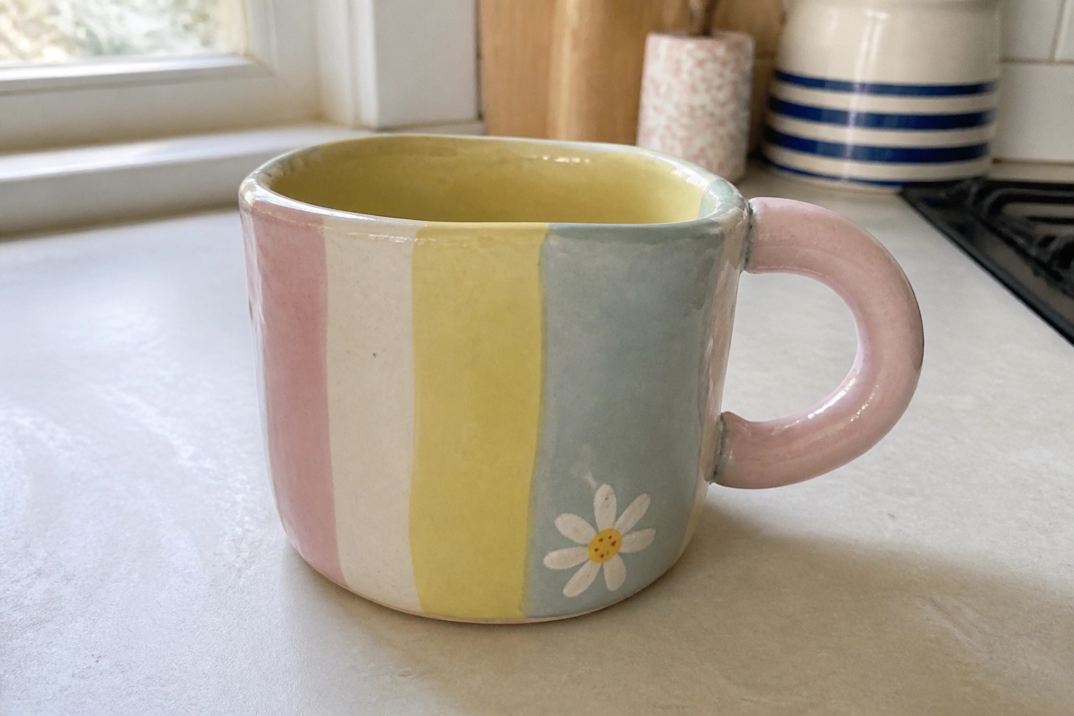 Striped ceramic mug with daisy on speckled kitchen countertop