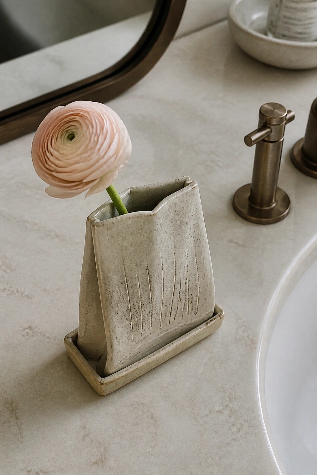 Pink ranunculus in speckled ceramic vase on marble bathroom countertop