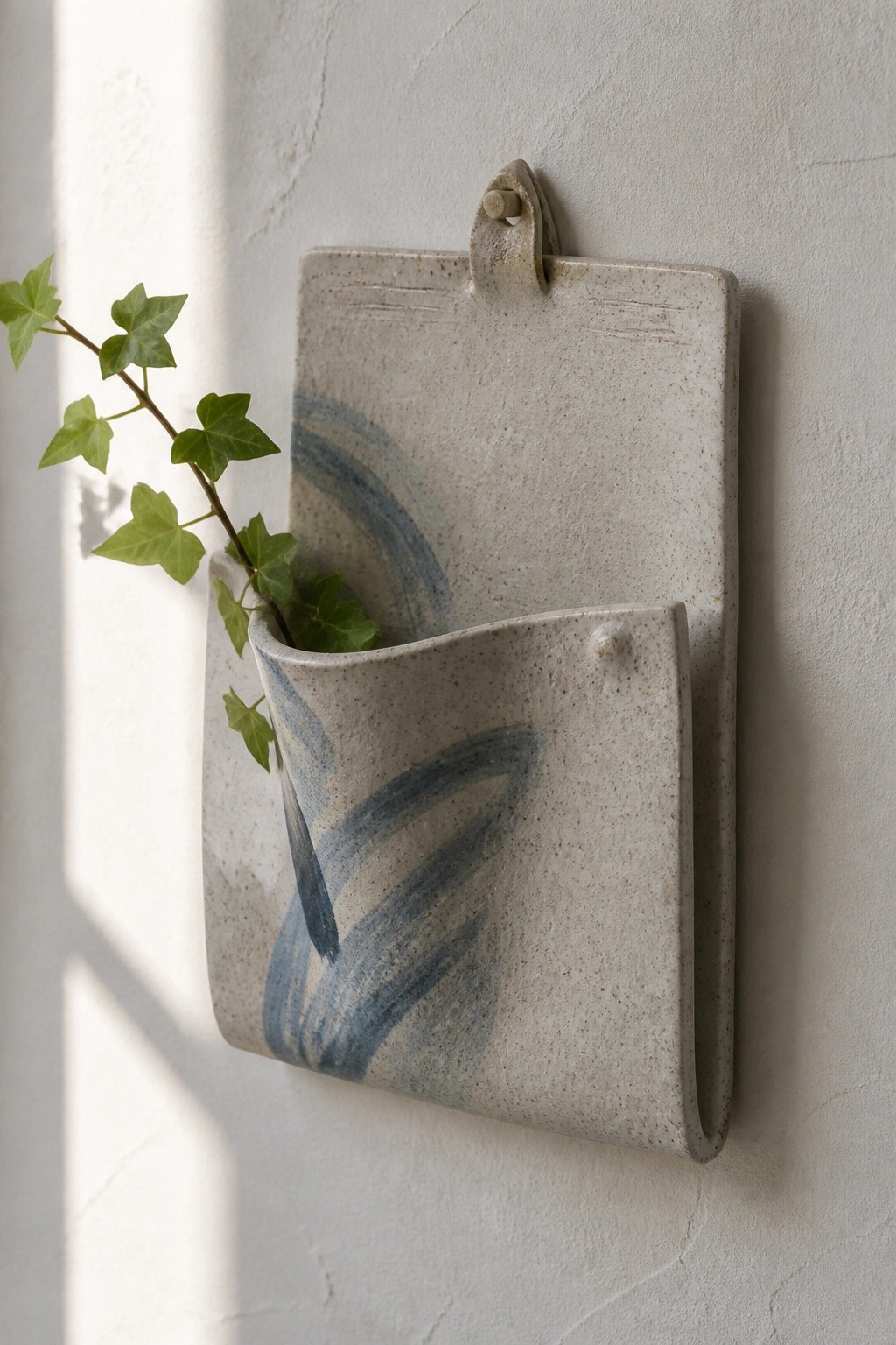 Ceramic wall pocket with blue brushstrokes holding trailing green ivy on textured wall