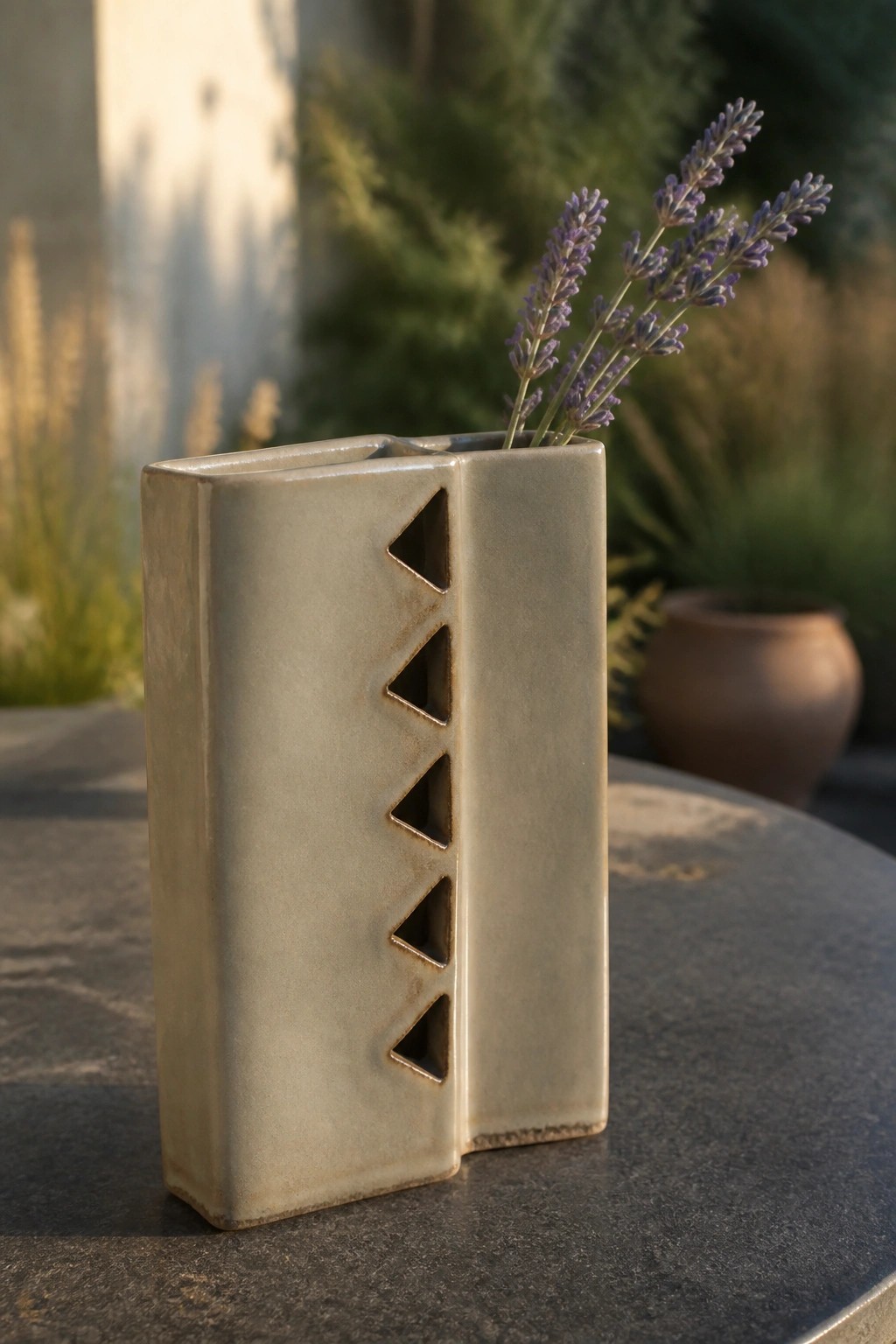 Matte rectangular ceramic vase with triangular cutouts holding lavender on stone table