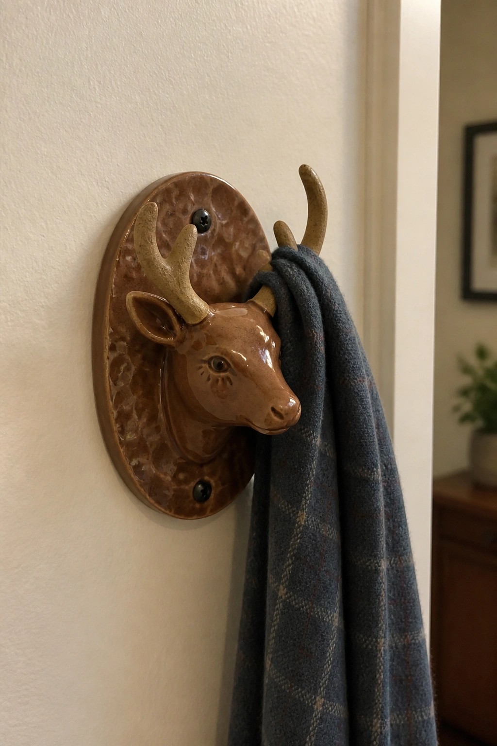Brown ceramic deer head hook on wall holding blue plaid scarf