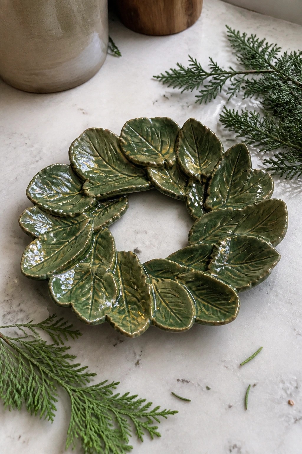 Green ceramic leaf wreath dish on white marble with evergreen sprigs