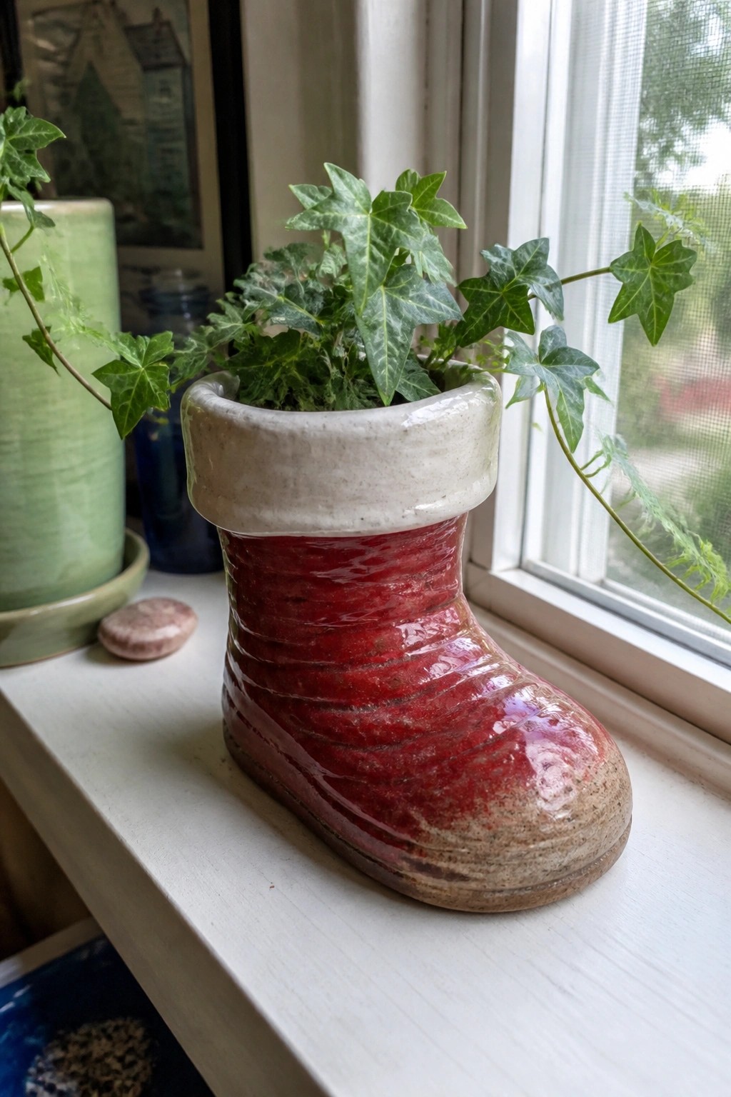 Red ceramic boot planter with green ivy on white windowsill by window