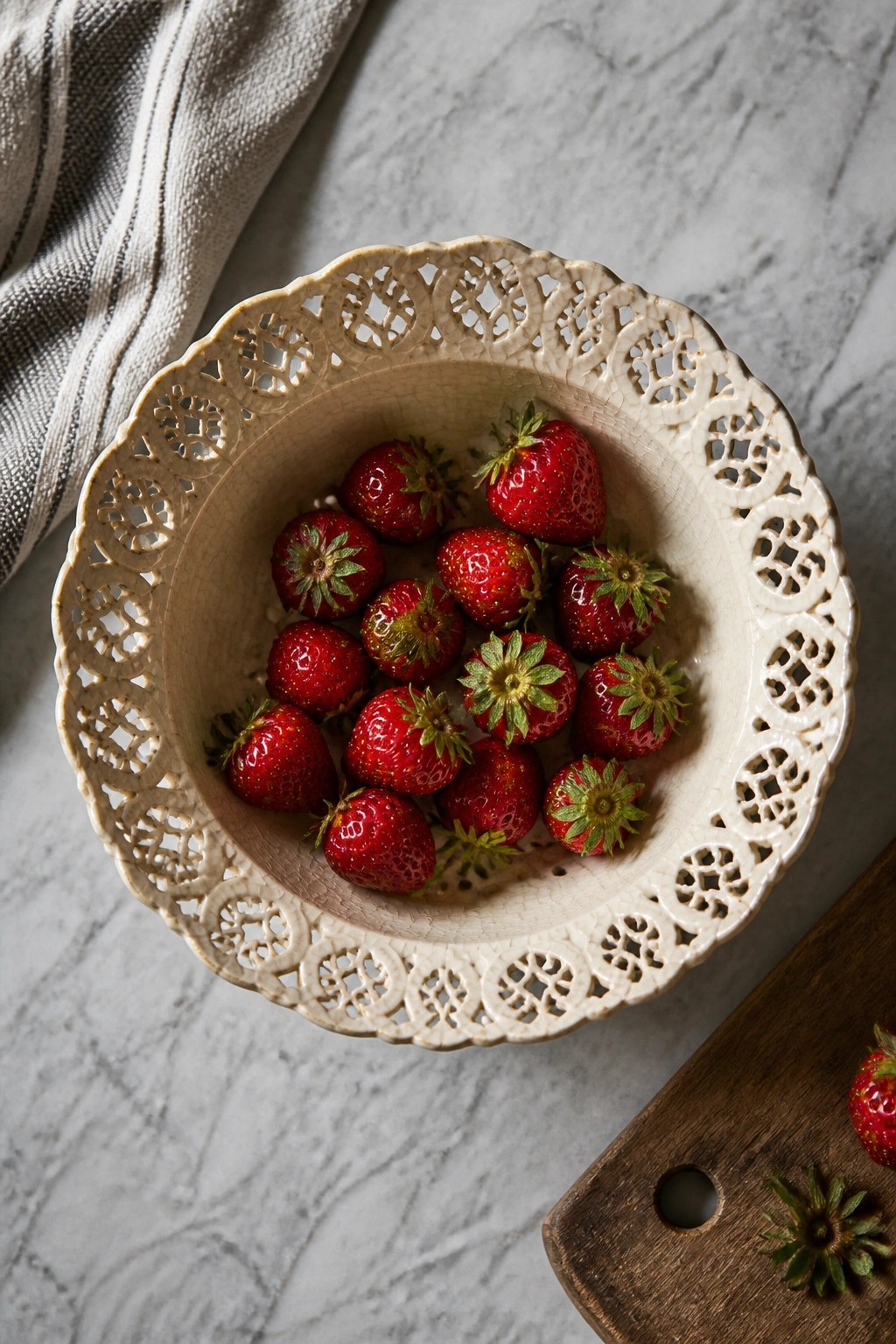 Fresh red strawberries in ornate white ceramic bowl on marble with linen cloth