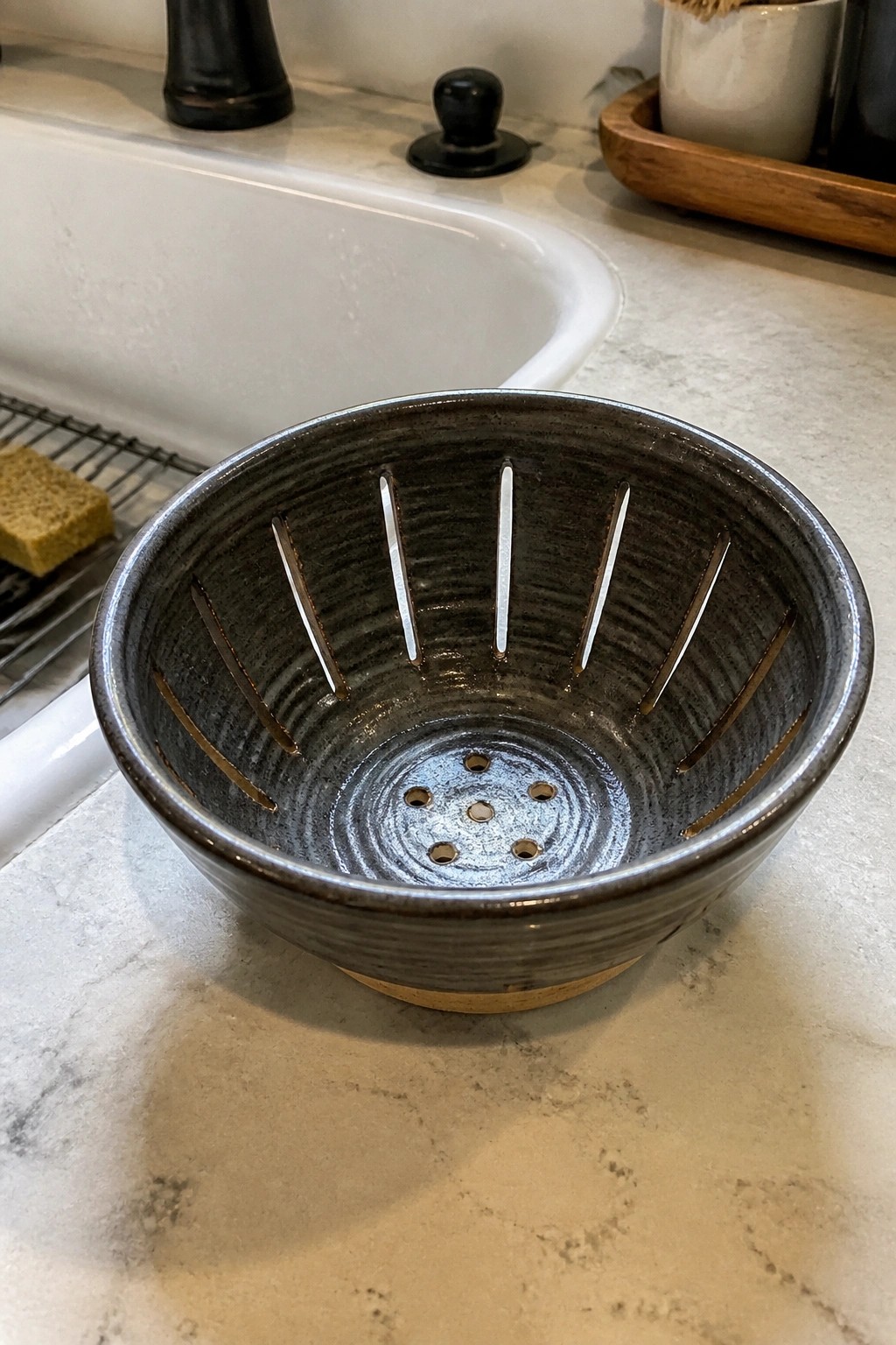 Dark ceramic bowl with vertical slits and bottom holes on marble counter