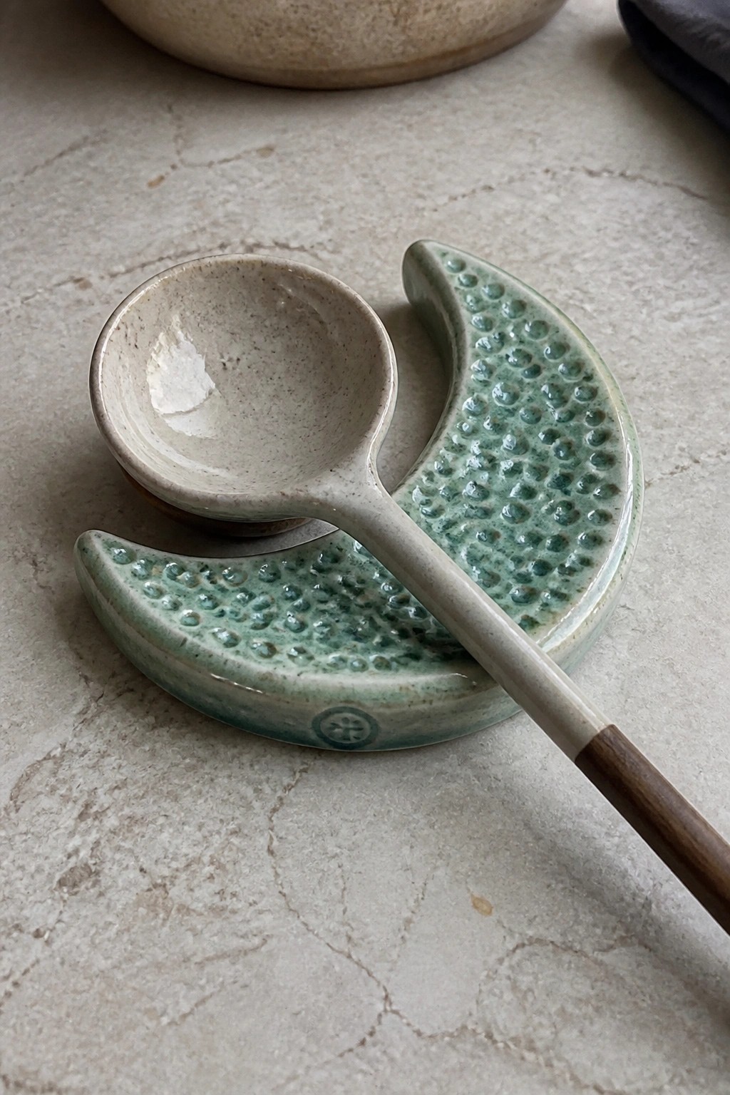 Ceramic spoon with wooden handle on green bumpy crescent rests