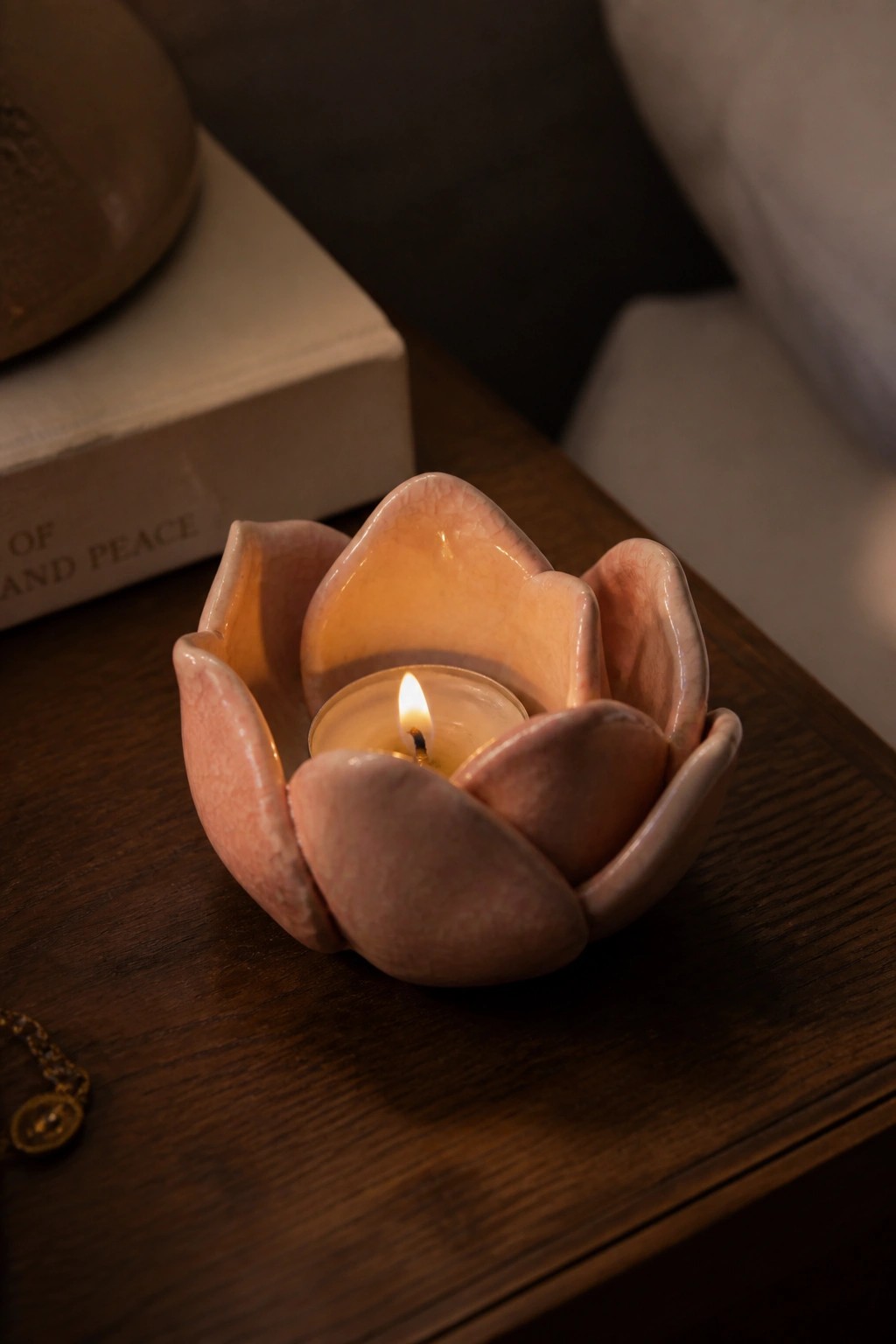 Lit tea light candle in pink lotus ceramic holder on dark wooden table